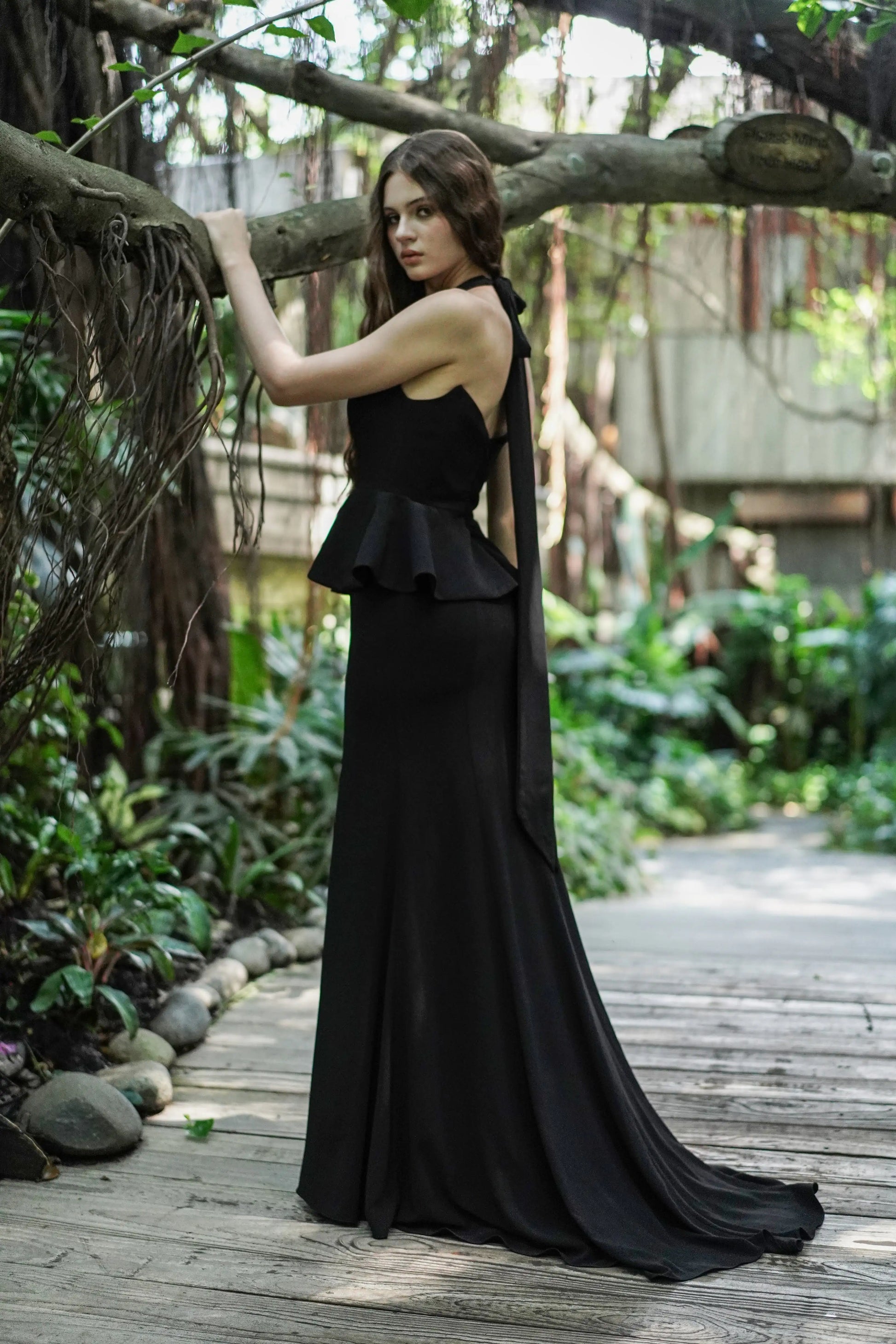 Woman wearing black peplum dress side view with train on skirt.