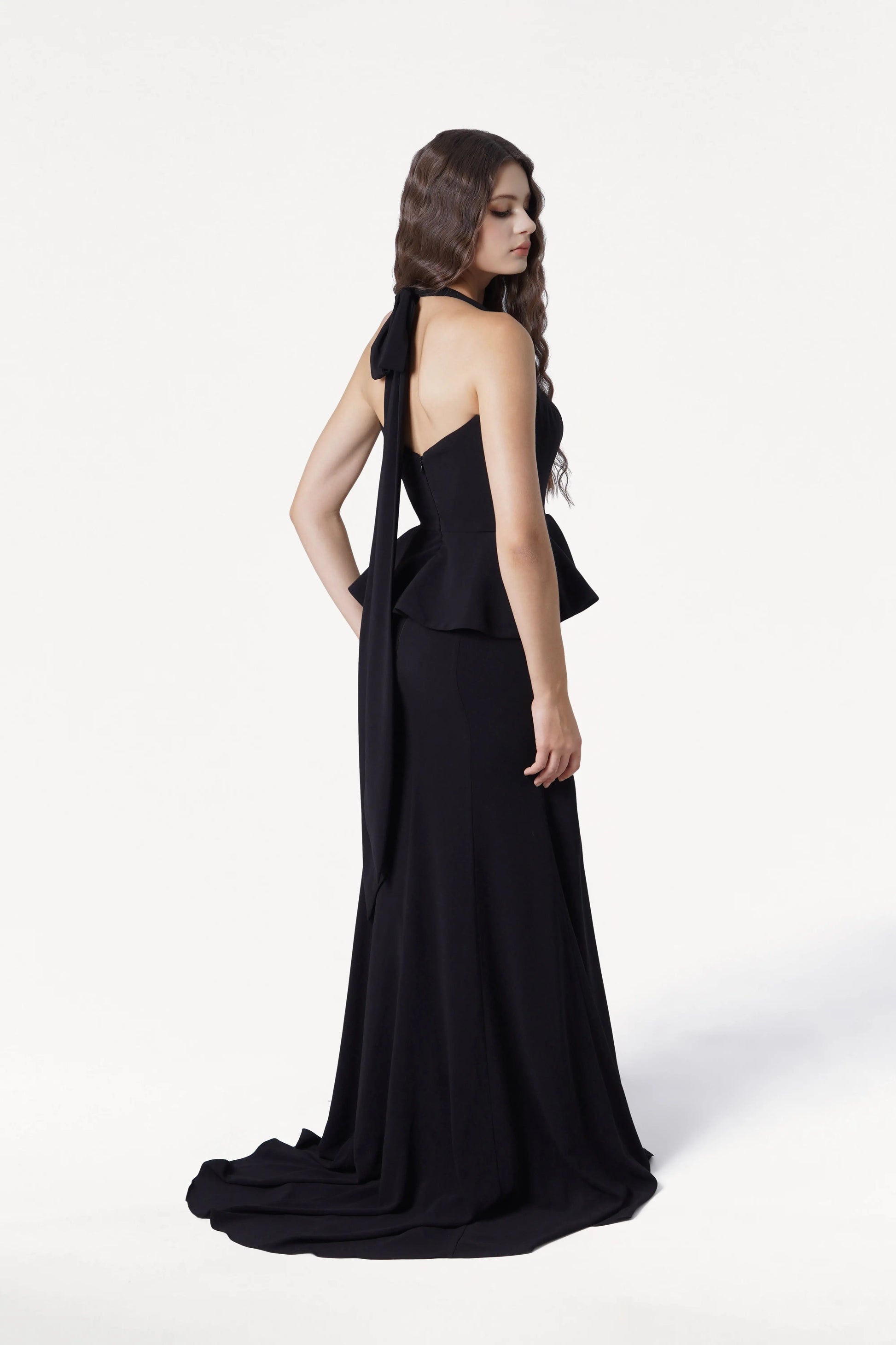 Woman wearing a black evening gown with a flowing train on a white background