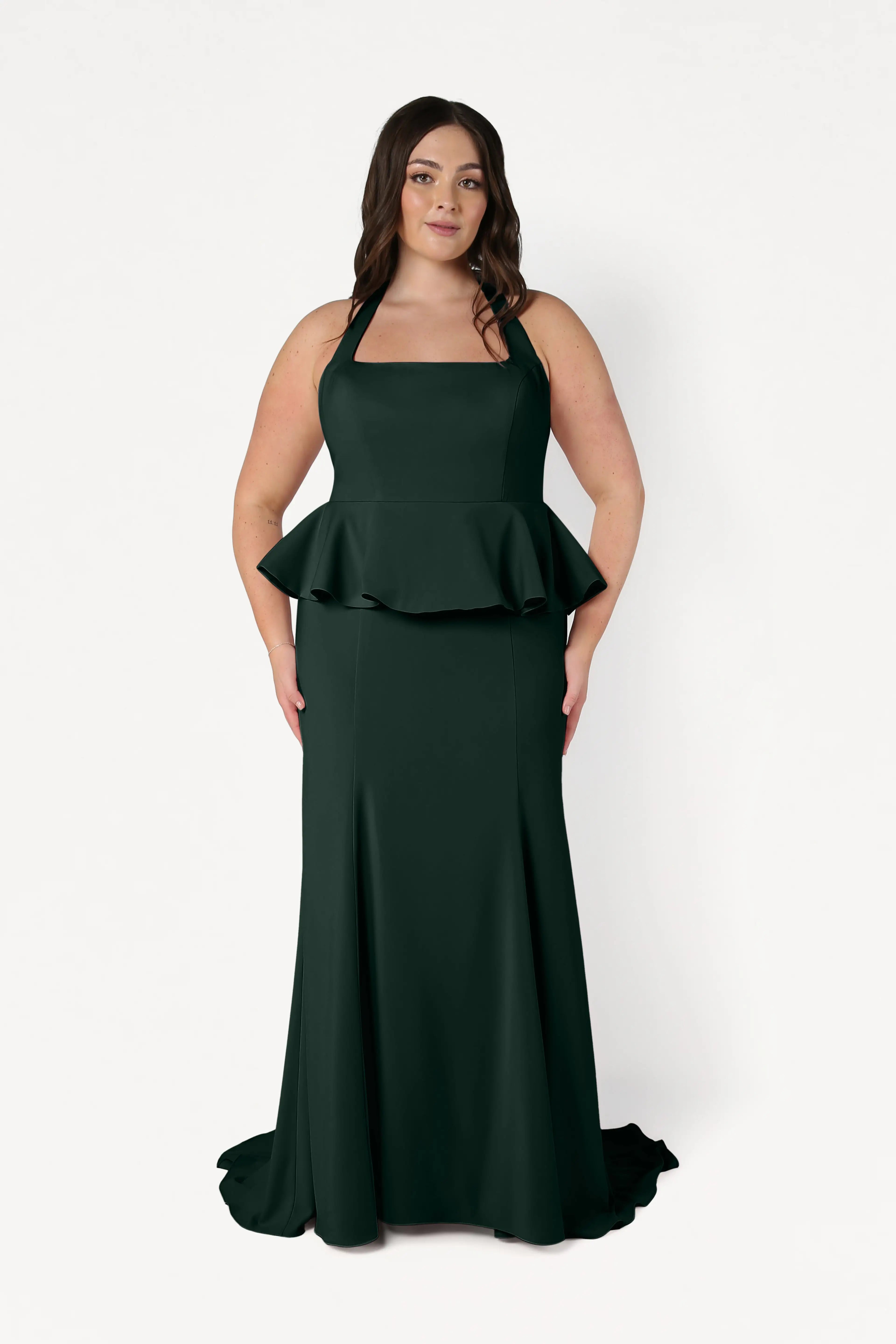 A woman stands against a plain white background wearing the TH&TH Peony Bridesmaid Dress in Forest Green, a sleeveless moss crepe gown with a square neckline, peplum waist, and floor-length skirt.