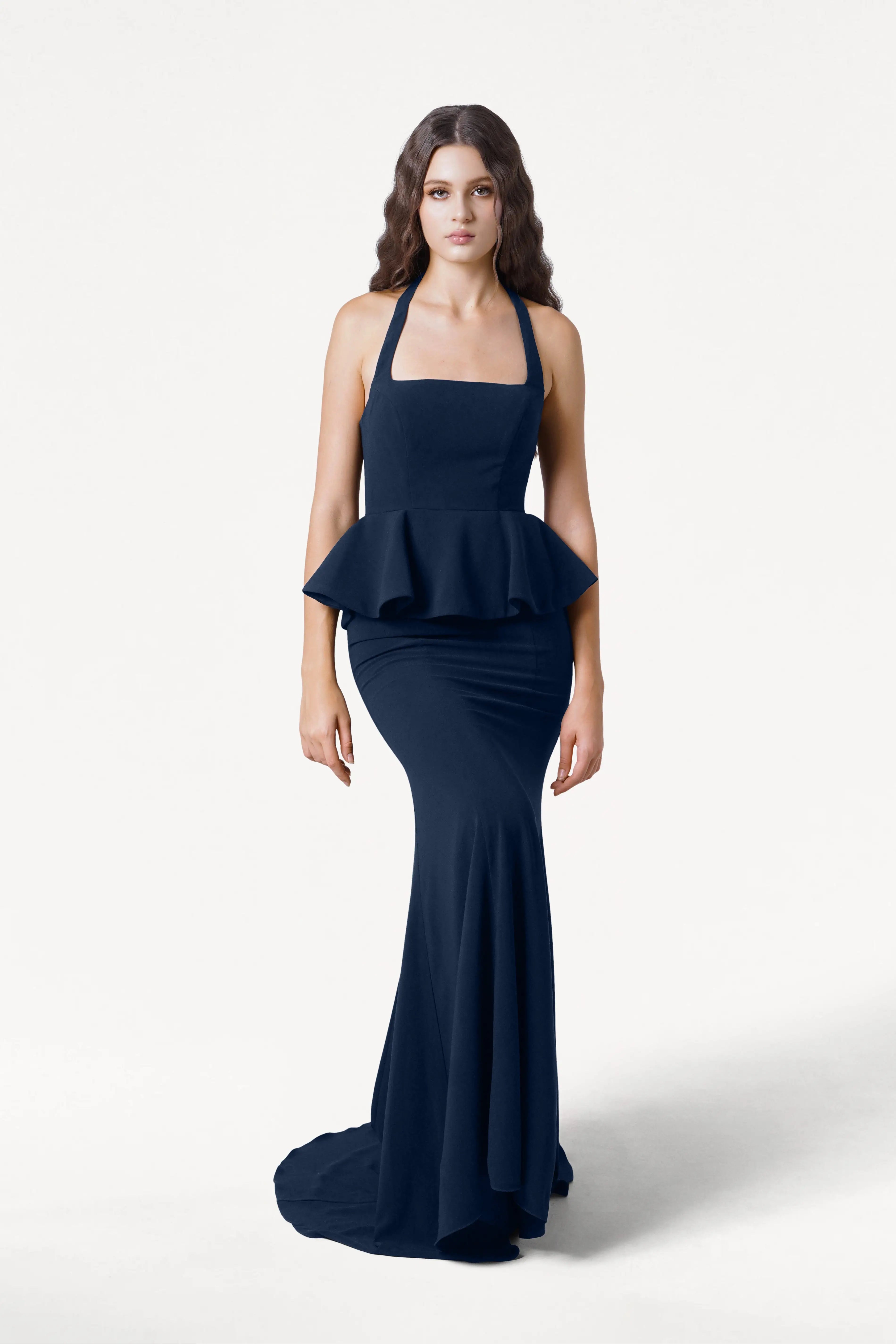 A woman with long wavy hair wears the TH&TH Peony Bridesmaid Dress in Navy, featuring a sleeveless design, peplum waist, and mermaid skirt, standing against a plain white background.