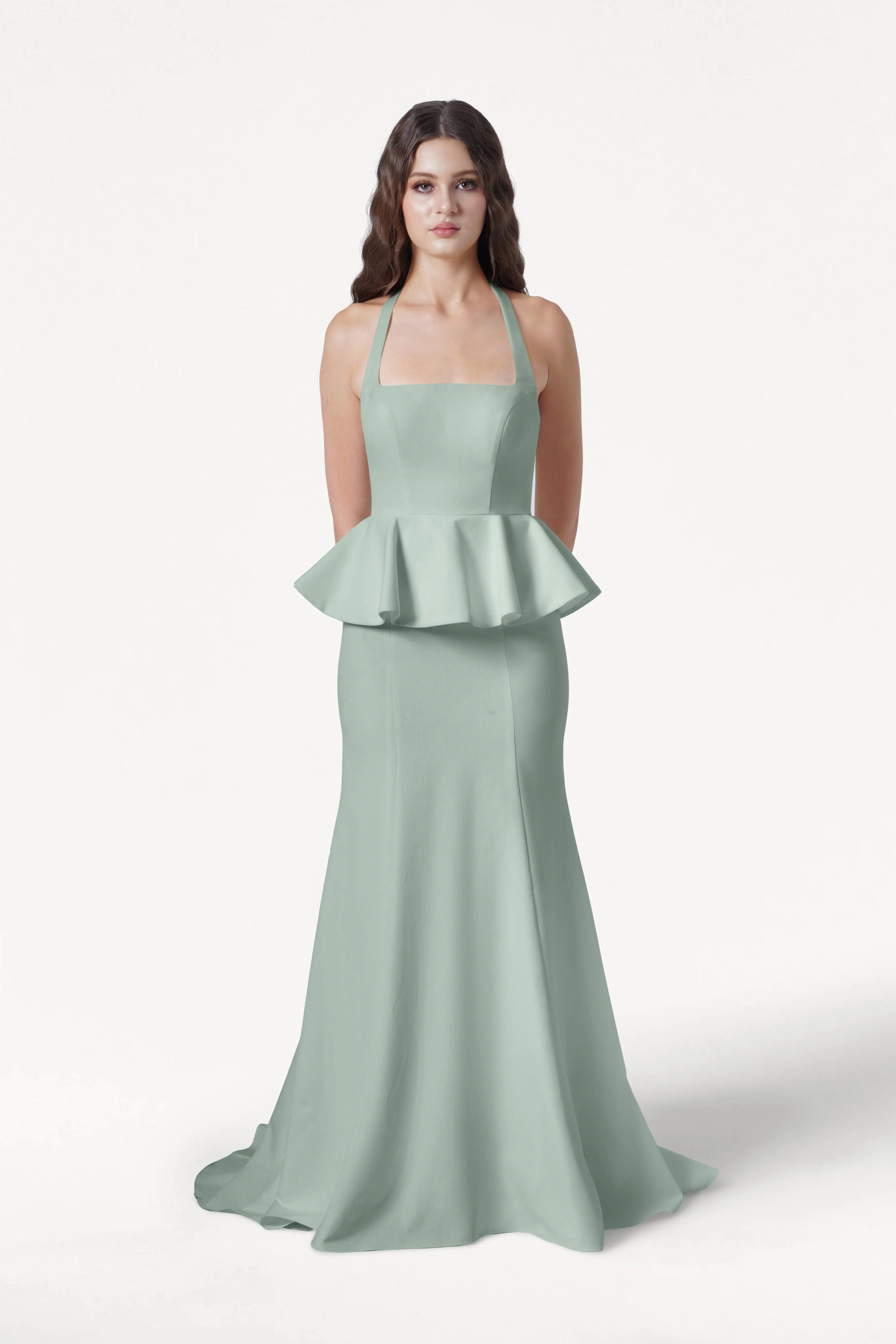 A woman faces forward in the Peony Bridesmaid Dress in Sage Green by TH&TH, featuring a halter neckline, peplum waist detail, and a floor-length moss crepe skirt against a plain white background.