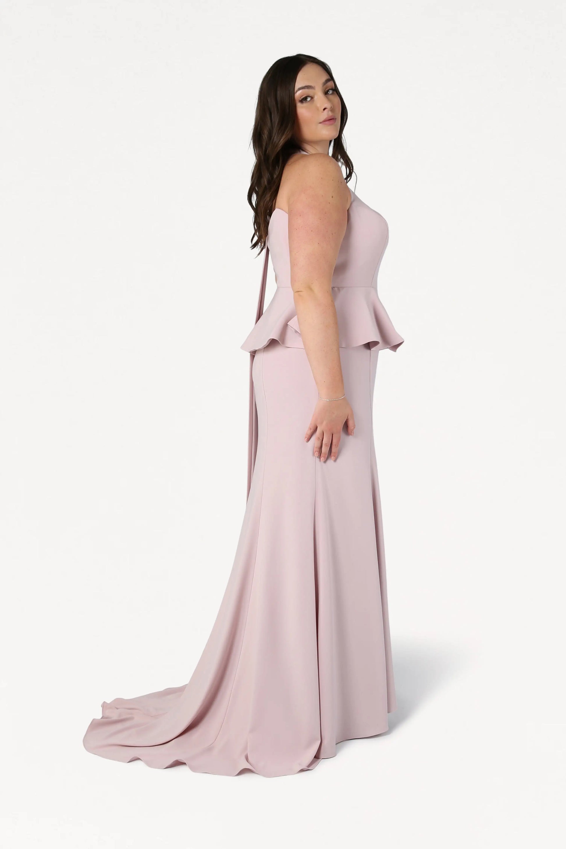 A woman with long brown hair models the TH&TH Peony Bridesmaid Dress in Smoked Blush, a size-inclusive, strapless gown with a fitted bodice and floor-length flared skirt, against a plain white background.