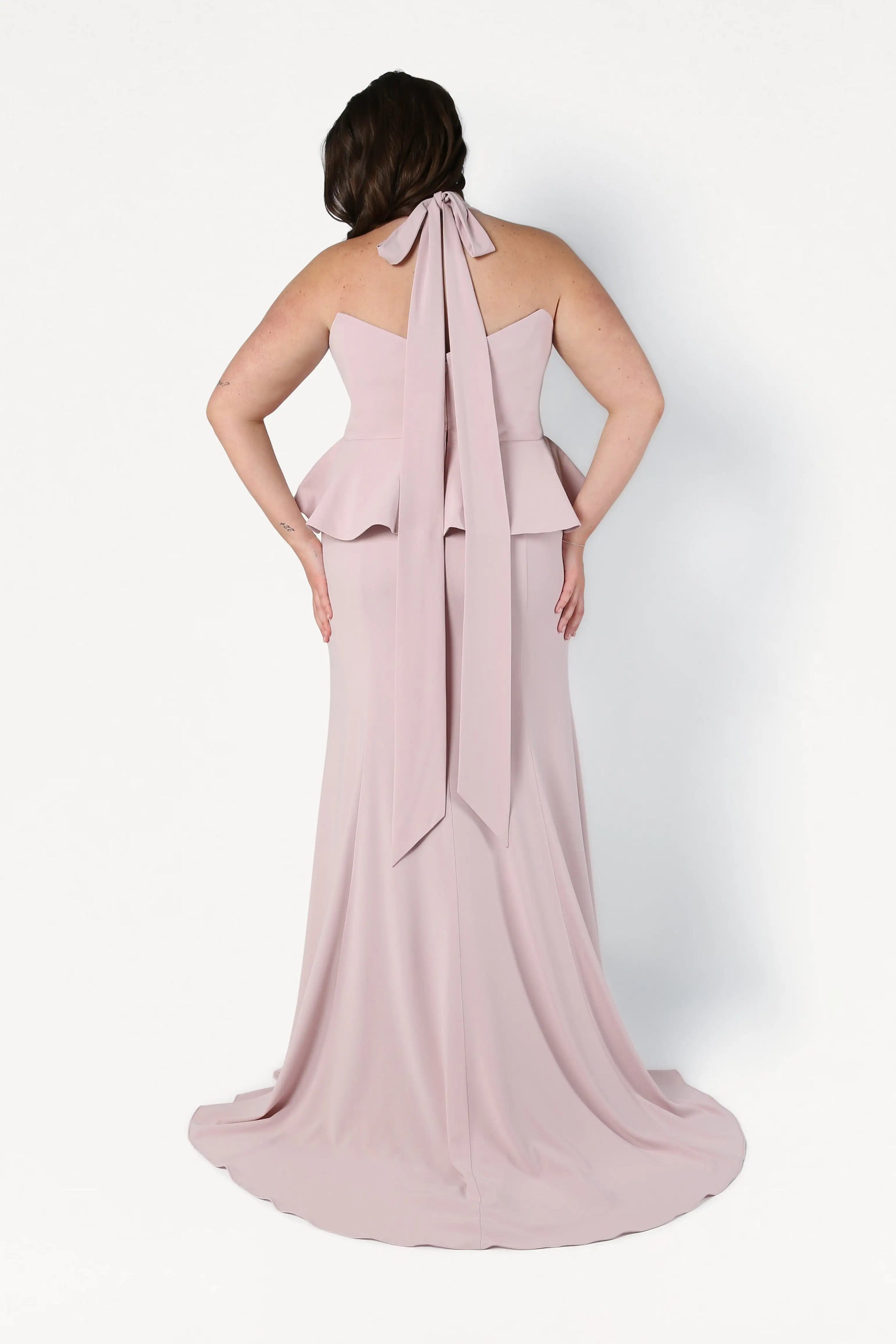 Woman wearing a pink halter neck gown with a large bow detail on a white background