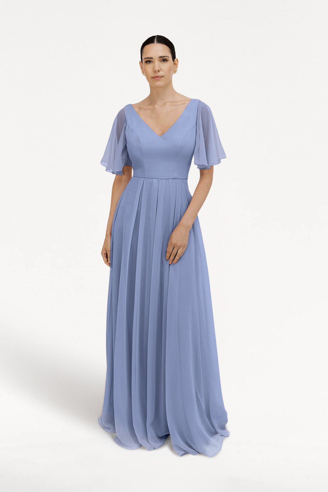 A woman wears the TH&TH Phoebe Bridesmaid Dress in French Blue chiffon, featuring a floor-length pleated skirt, flutter sleeves, and a V-neckline, standing against a plain white background.