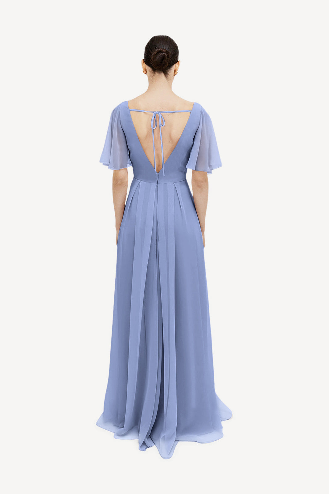 Back view of a woman in the TH&TH Phoebe Bridesmaid Dress in French Blue Chiffon, featuring flutter sleeves, a deep V-back with tie detail, and a flowing pleated skirt—an elegant choice for bridesmaids.