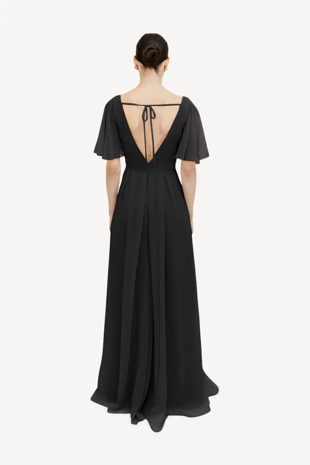 A woman is shown from the back in the TH&TH Phoebe Bridesmaid Dress in black chiffon, featuring flutter sleeves, a deep V-back with a tie at the top, and a flowing floor-length skirt ideal for maternity wear.