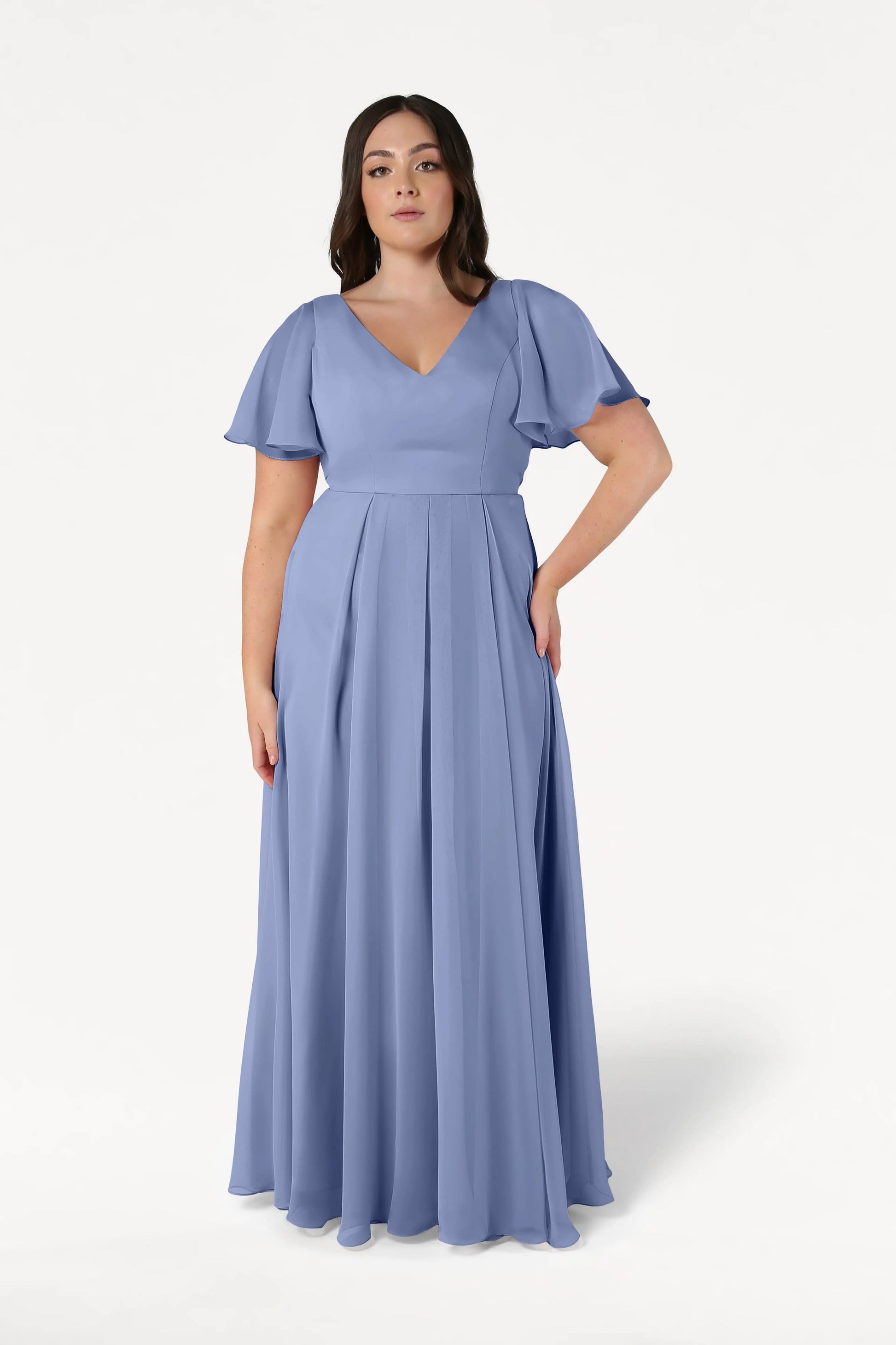 A woman wears the TH&TH Phoebe Bridesmaid Dress in French Blue Chiffon, a floor-length gown with short flutter sleeves and a V-neckline, standing against a plain white background.