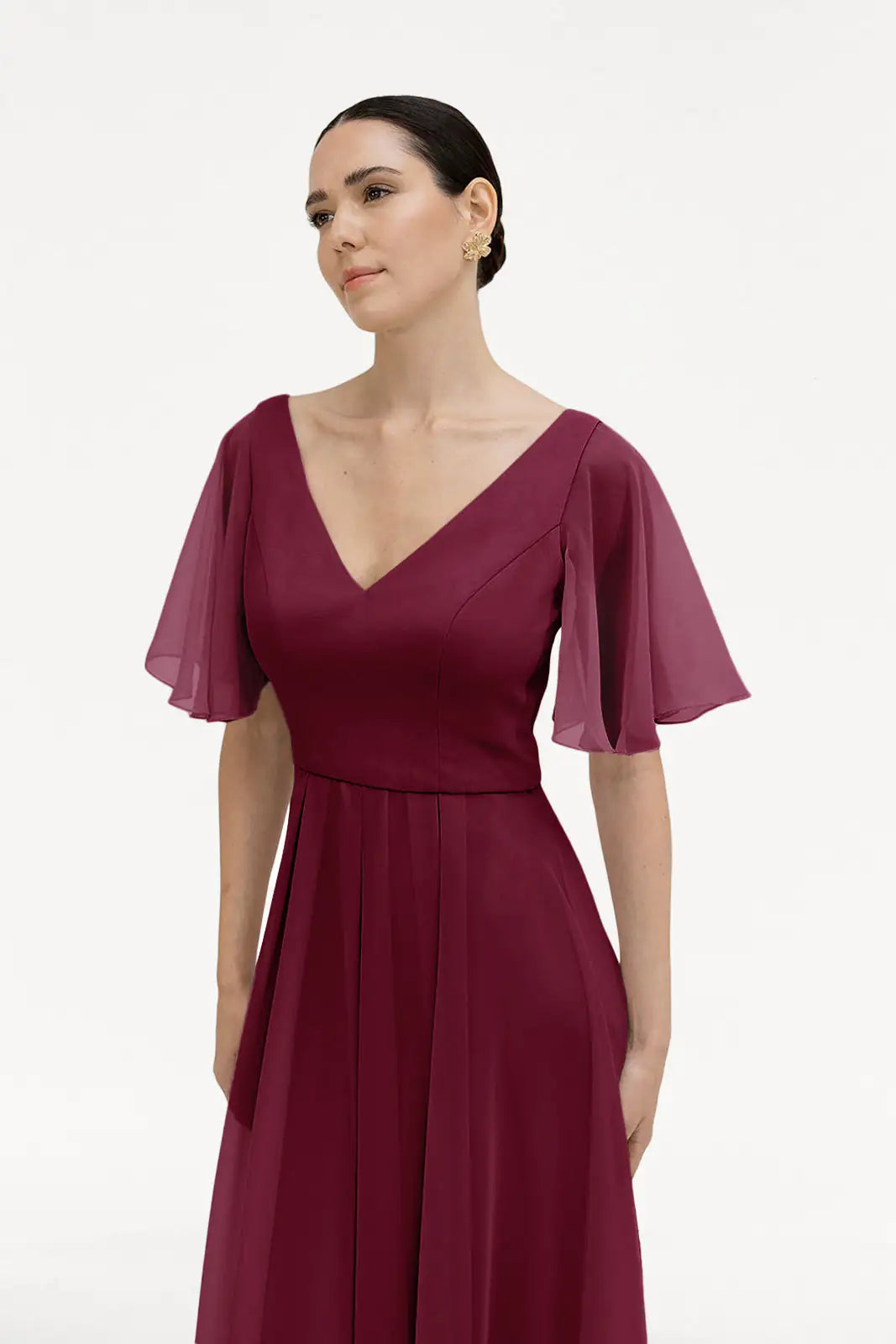 A woman in the TH&TH Phoebe Bridesmaid Dress in Merlot Chiffon, featuring a V-neckline and sheer flutter sleeves, stands against a white background with her dark hair pulled back. This elegant gown is a stunning bridesmaid choice.