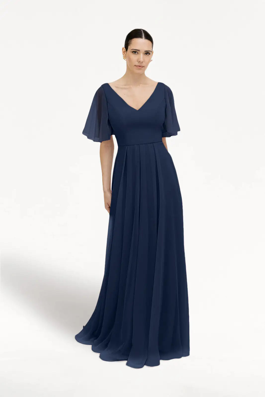 A woman models the TH&TH Phoebe Bridesmaid Dress in Navy Chiffon, a floor-length gown with a V-neckline and short flutter sleeves—an elegant, bump-friendly choice for bridesmaids.