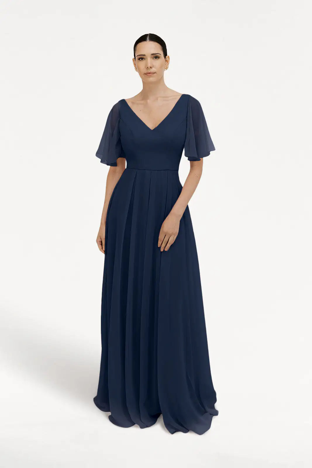 A woman wears the TH&TH Phoebe Bridesmaid Dress in Navy Chiffon, a floor-length gown with short sheer flutter sleeves and a V-neckline, styled bump-friendly, against a plain white background with her hair parted and pulled back.