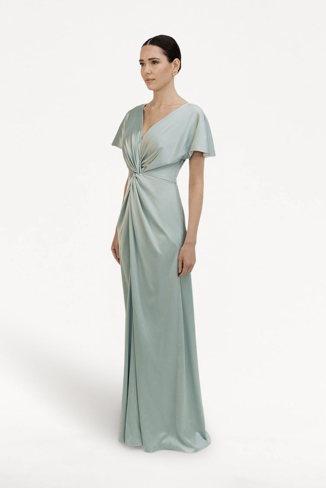 A woman with dark hair pulled back models the TH&TH Camilla Bridesmaid Dress in Dusty Eucalyptus Satin, featuring short sleeves and a twist-knot waist, standing against a plain white background.