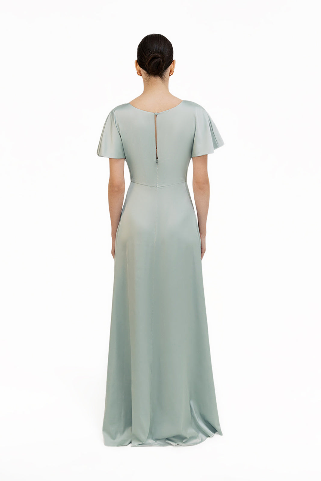 A woman stands facing away, wearing the TH&TH Camilla Bridesmaid Dress in Dusty Eucalyptus Satin—an inclusive floor-length gown with short flutter sleeves and a keyhole back detail—set against a plain white background.
