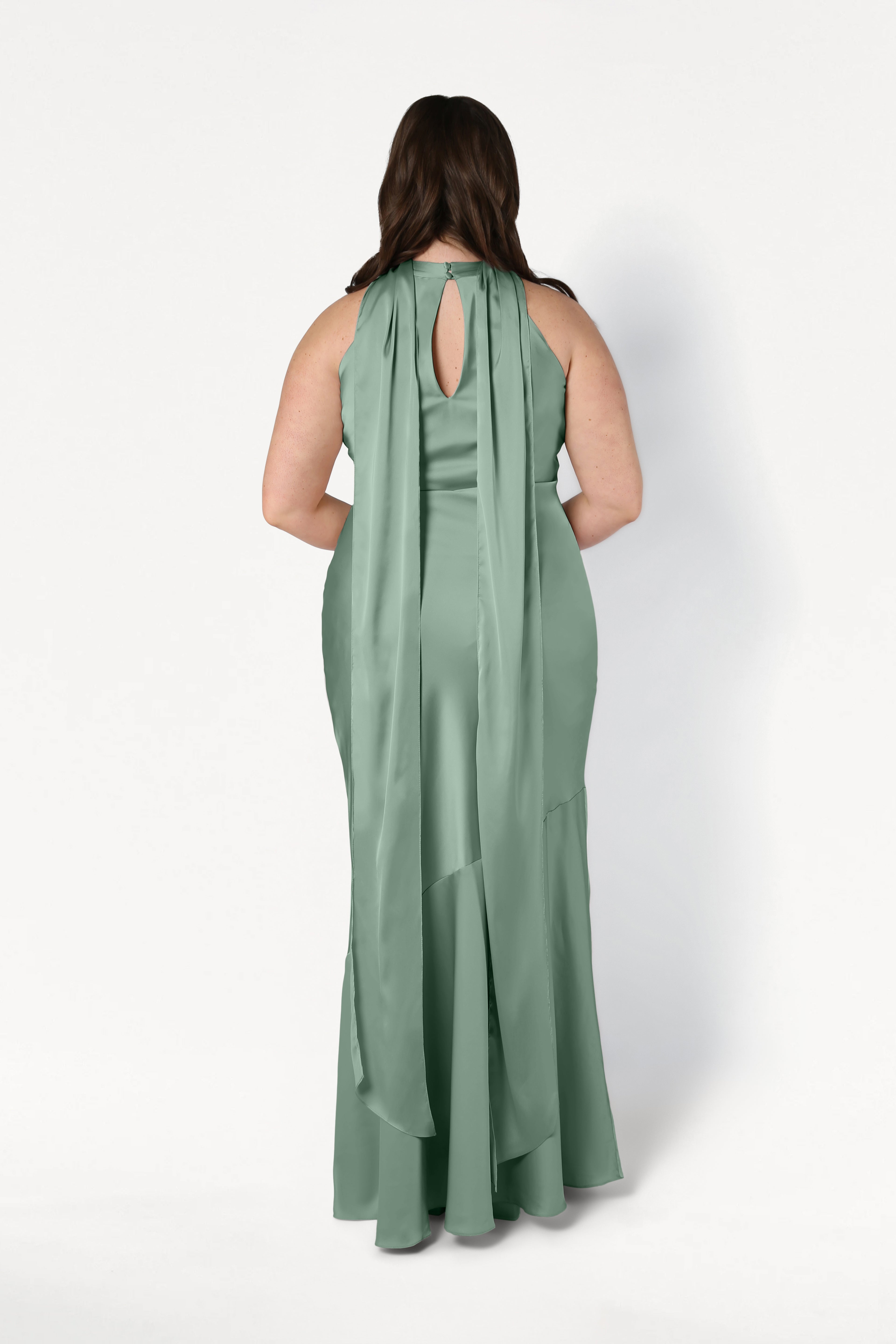 A woman is shown from the back wearing the TH&TH Mira Bridesmaid Dress in Sage Green Satin, a floor-length gown with an upper-back keyhole cutout and two long sashes over the skirt, against a plain white background.