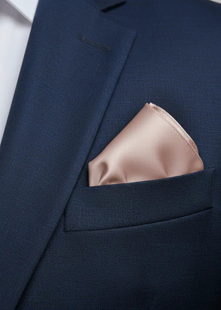 Close-up of a navy blue suit jacket with a white shirt, featuring a light pink TH&TH Satin Pocket Square neatly folded in the breast pocket.