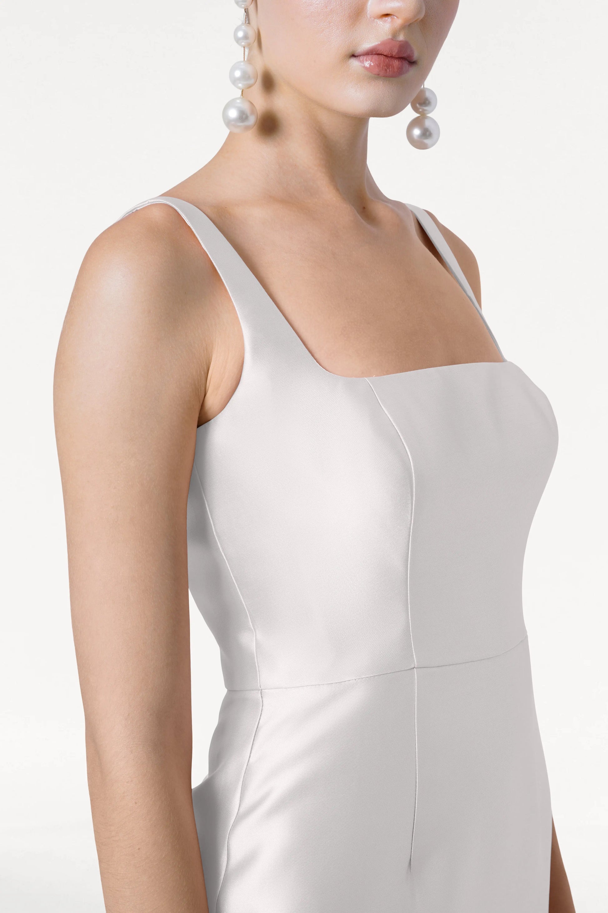 Close-up of a woman wearing the TH&TH Savoy Dress in Ivory Satin Twill, featuring a modern square neckline and structured bodice, styled with oversized pearl drop earrings against a neutral background.
