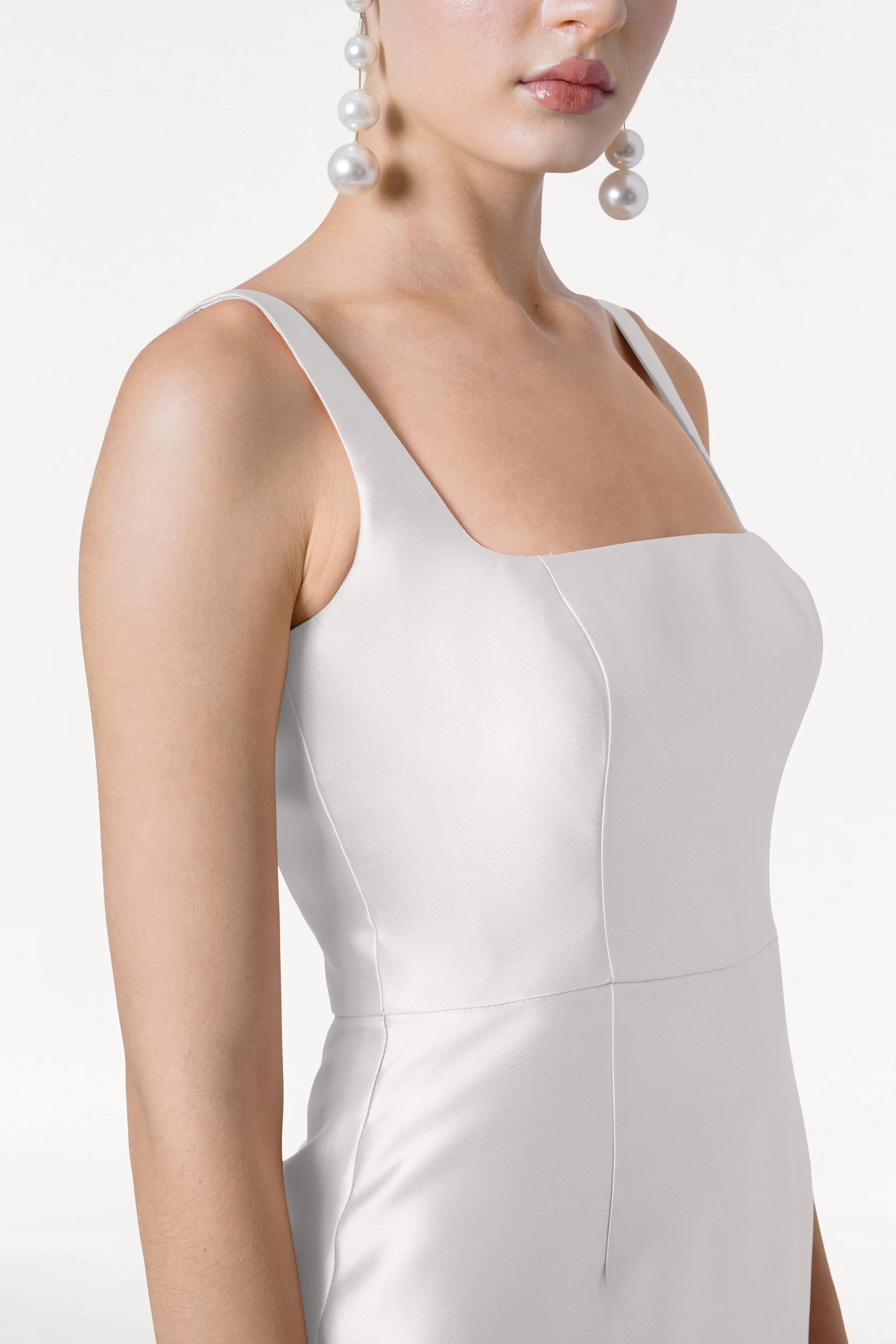 Close-up of a woman wearing the TH&TH Savoy Dress in Ivory Satin Twill, featuring a modern square neckline and structured bodice, styled with oversized pearl drop earrings against a neutral background.