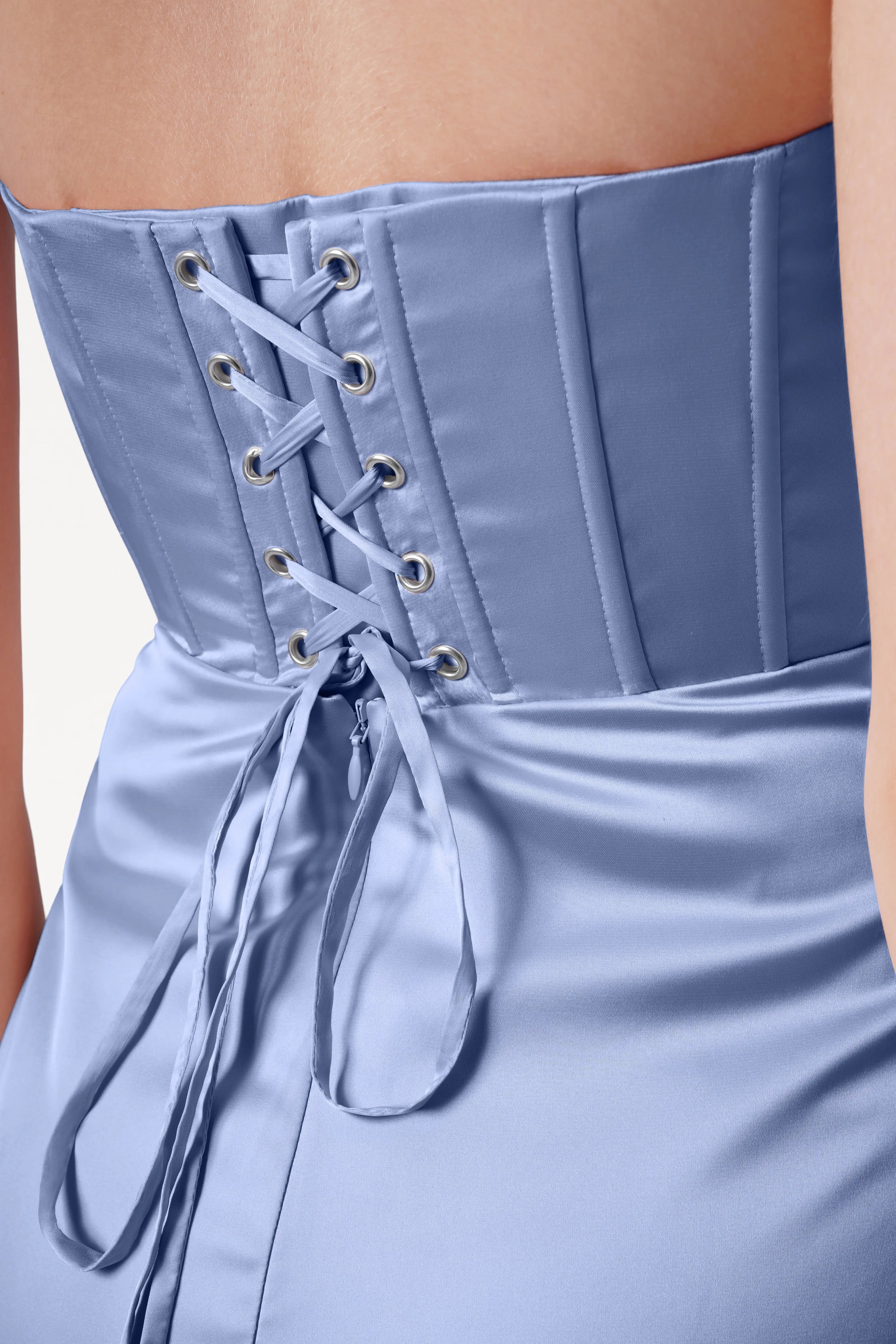 A close-up of a person wearing the Selena Bridesmaid Dress in French Blue Satin by TH&TH, featuring a corset-style lace-up back, vertical boning, and draped pleats that highlight the smooth, shiny fabric.