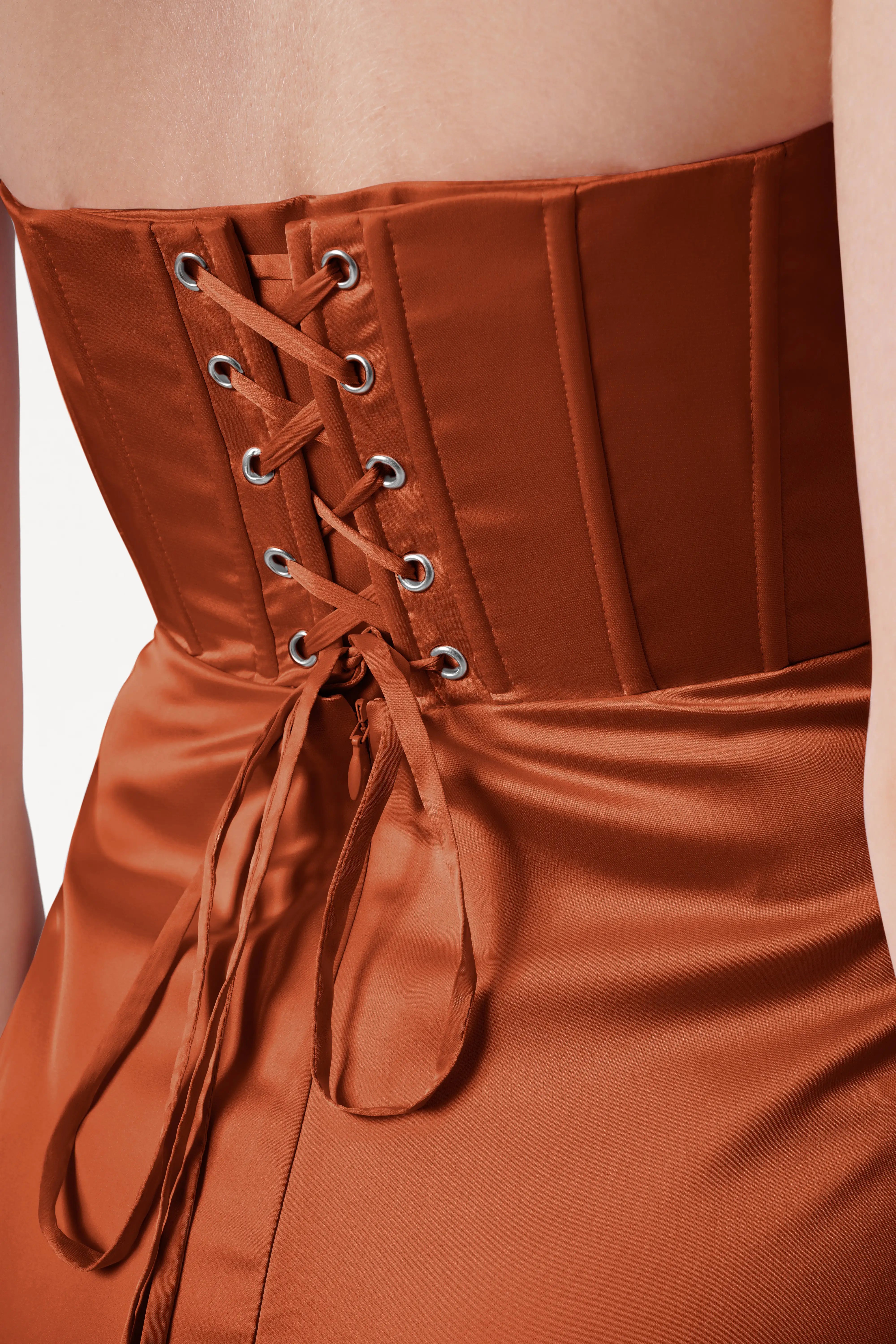 Close-up of a burnt orange satin corset with lace-up front on a beige background