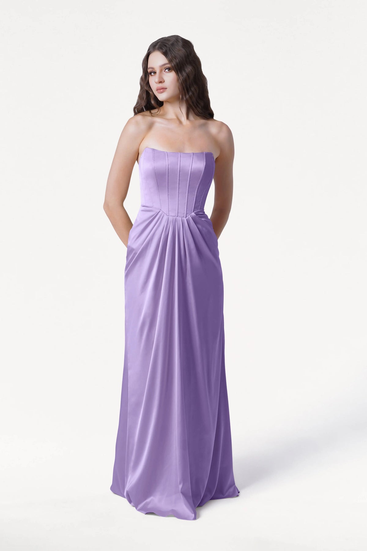A woman with long brown hair models the TH&TH Selena Bridesmaid Dress in Violet Satin, a strapless, floor-length gown with a fitted bodice and subtle waist pleating, standing against a plain white background.