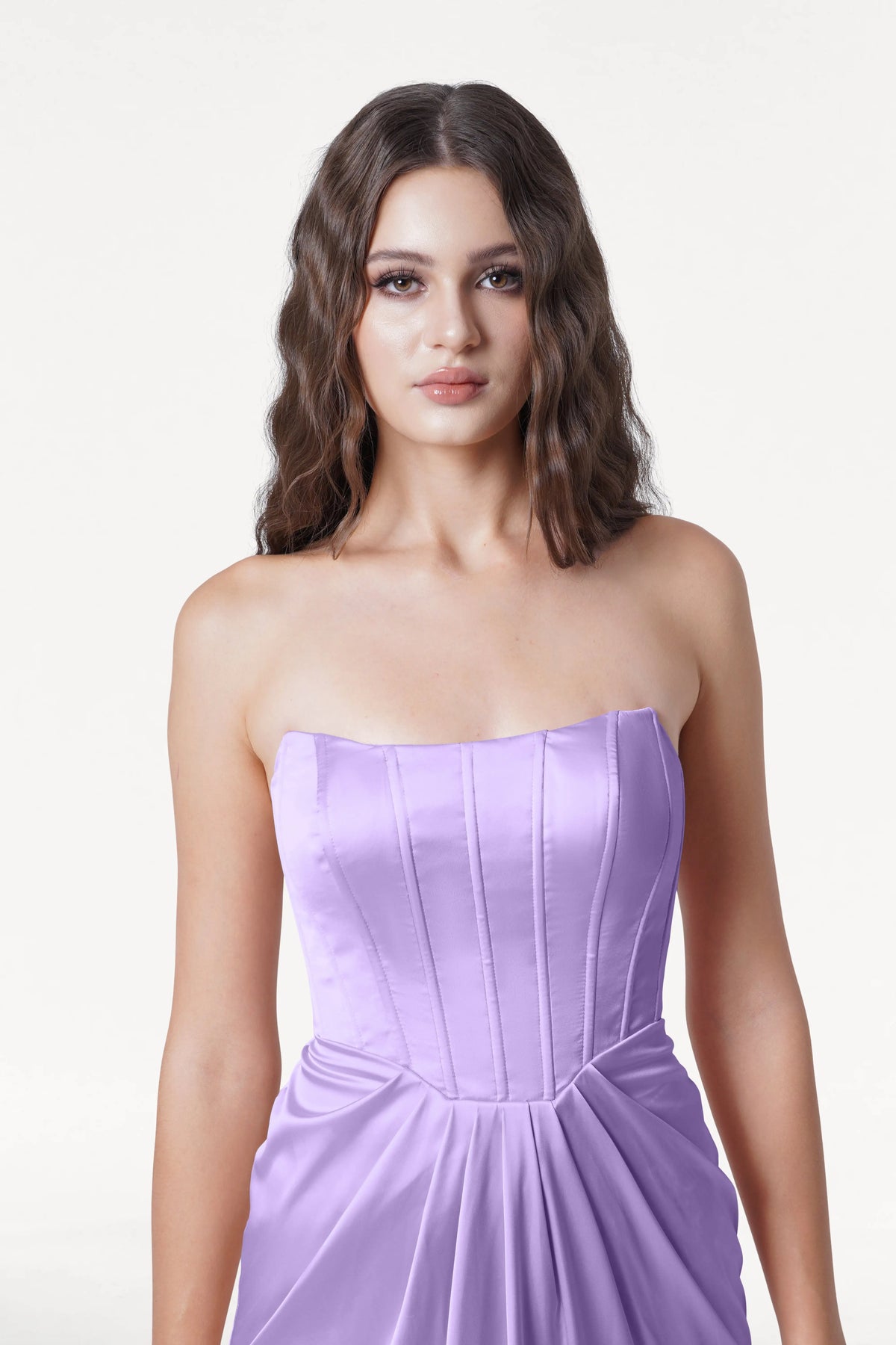 A woman with wavy brown hair models the TH&TH Selena Bridesmaid Dress in Violet Satin, a strapless gown with a corset bodice and gathered waist, posed against a plain white background.