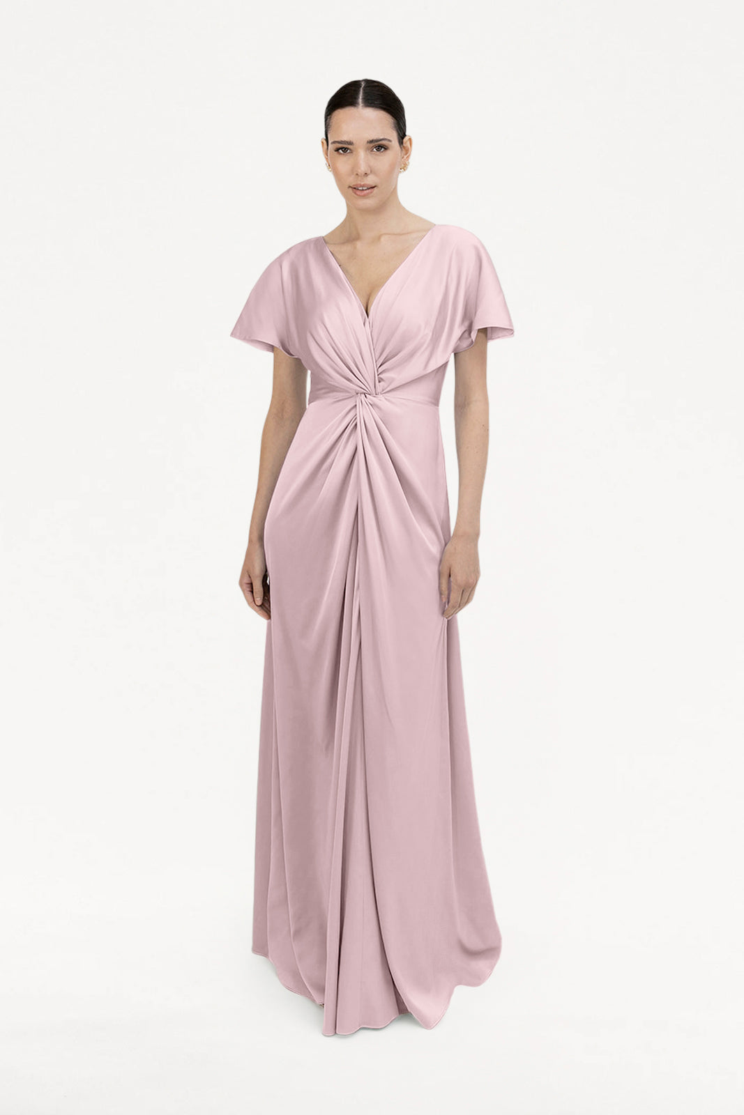 A woman stands against a white background wearing the TH&TH Camilla Bridesmaid Dress in Smoked Blush Satin, a floor-length gown featuring short sleeves, a deep V-neck, and a gathered twist detail at the waist and center front.