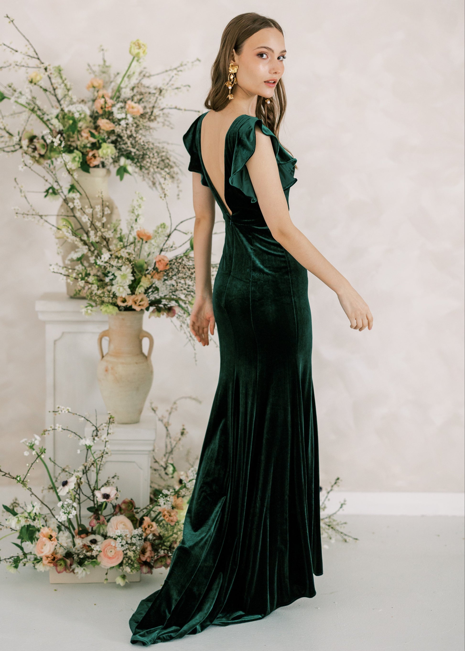 Woman in a green velvet dress standing next to floral arrangements against a light background