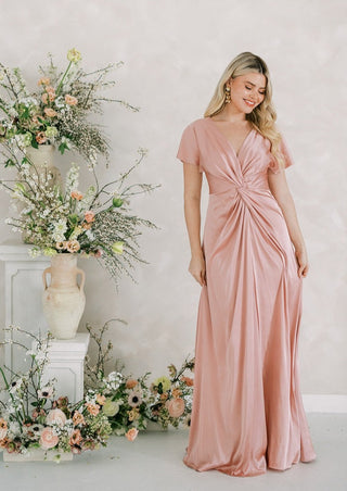 Blush pink satin maxi bridesmaid dress with flattering twist knot front detail and sleeves.
