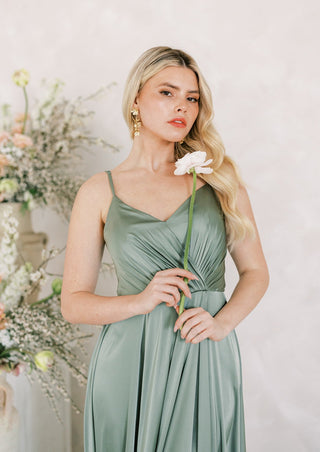 Sage green satin maxi bridesmaid dress with spaghetti straps and pleated bodice.