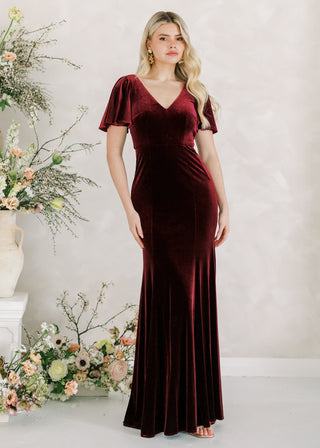 Woman in a burgundy dress standing next to floral arrangements on a white background