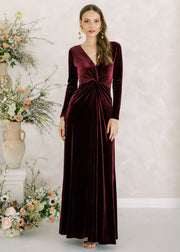 Woman in a burgundy velvet dress standing next to floral arrangements against a light background