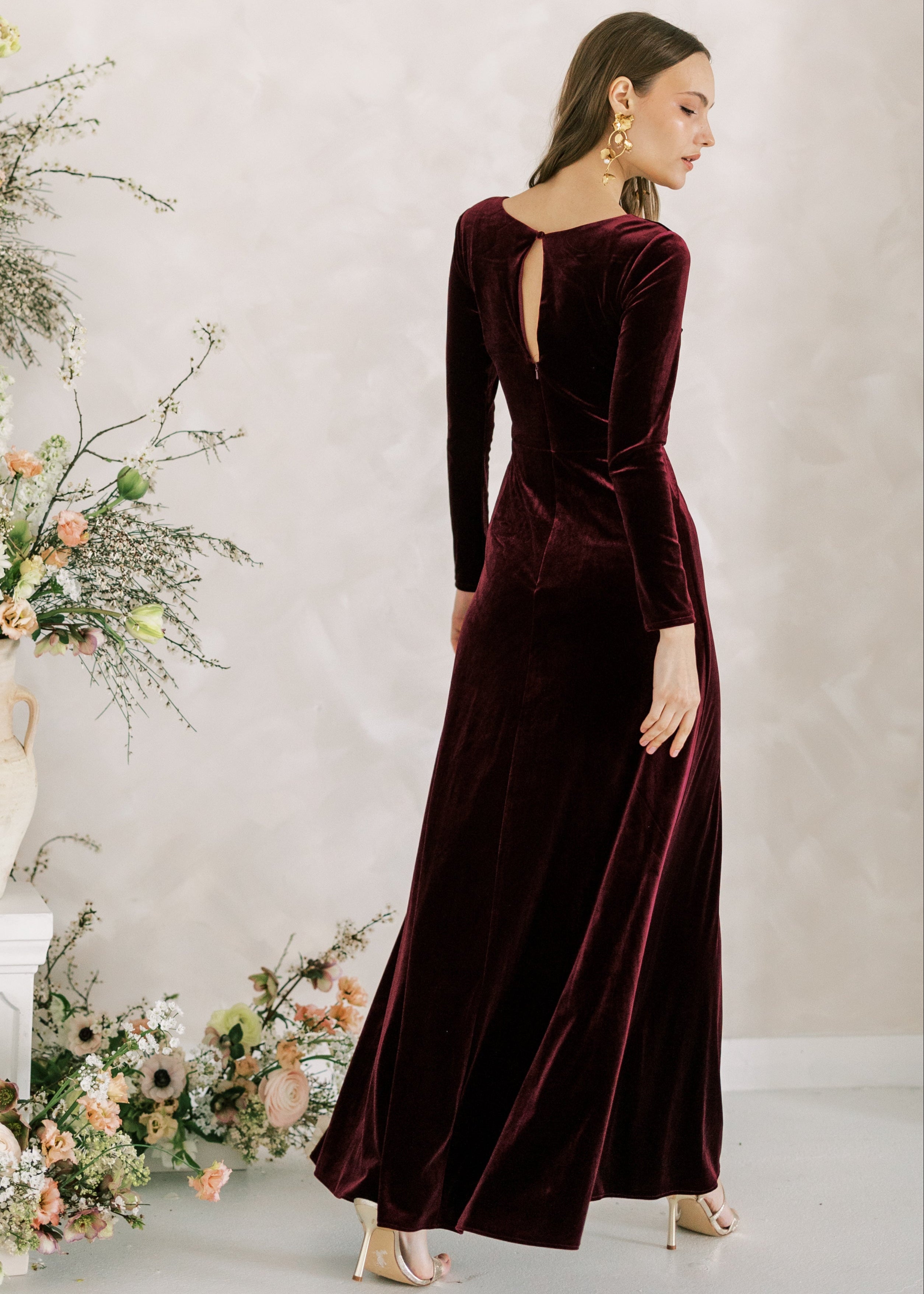 Woman wearing a burgundy velvet dress in a room with floral decorations.