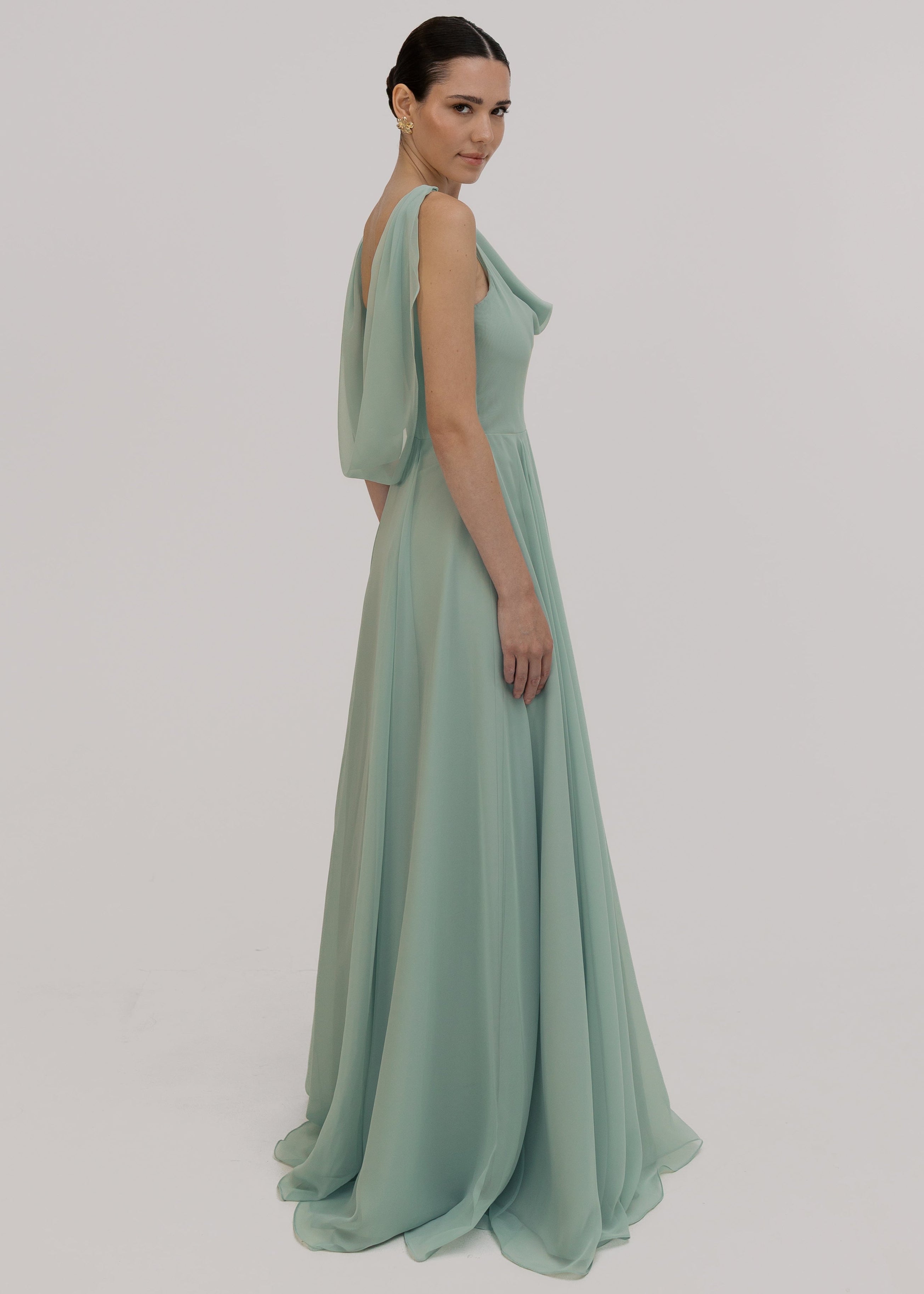 Model wearing a light green evening gown side view showing cowl back detail on a plain background by TH&TH.