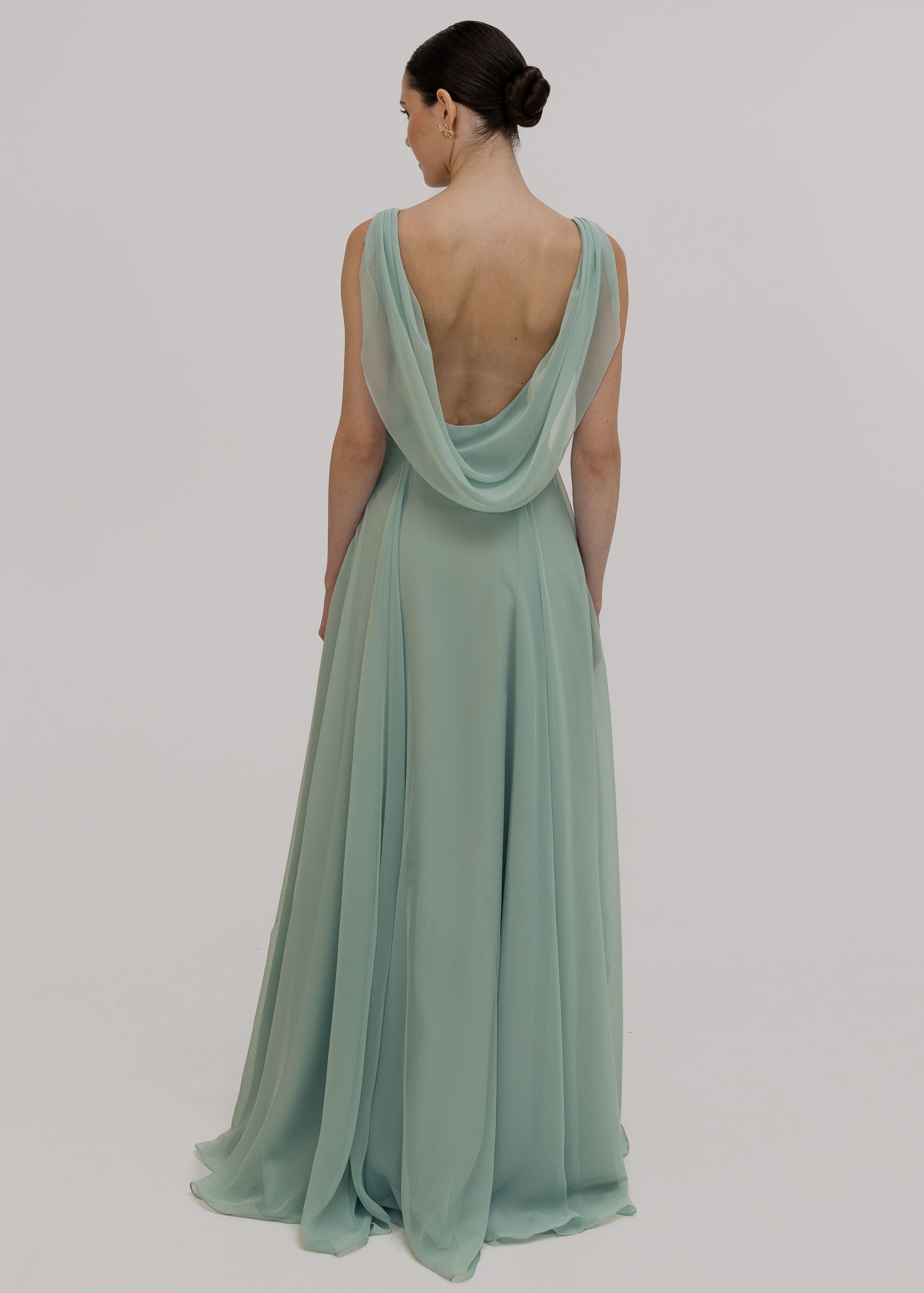 Woman wearing a light green bridesmaid dress with a low cowl back detail on a plain background by TH&TH Bridesmaids.
