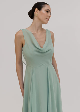 Woman wearing a light green dress with cowl neck detail against a plain background by TH&TH Bridesmaids. 