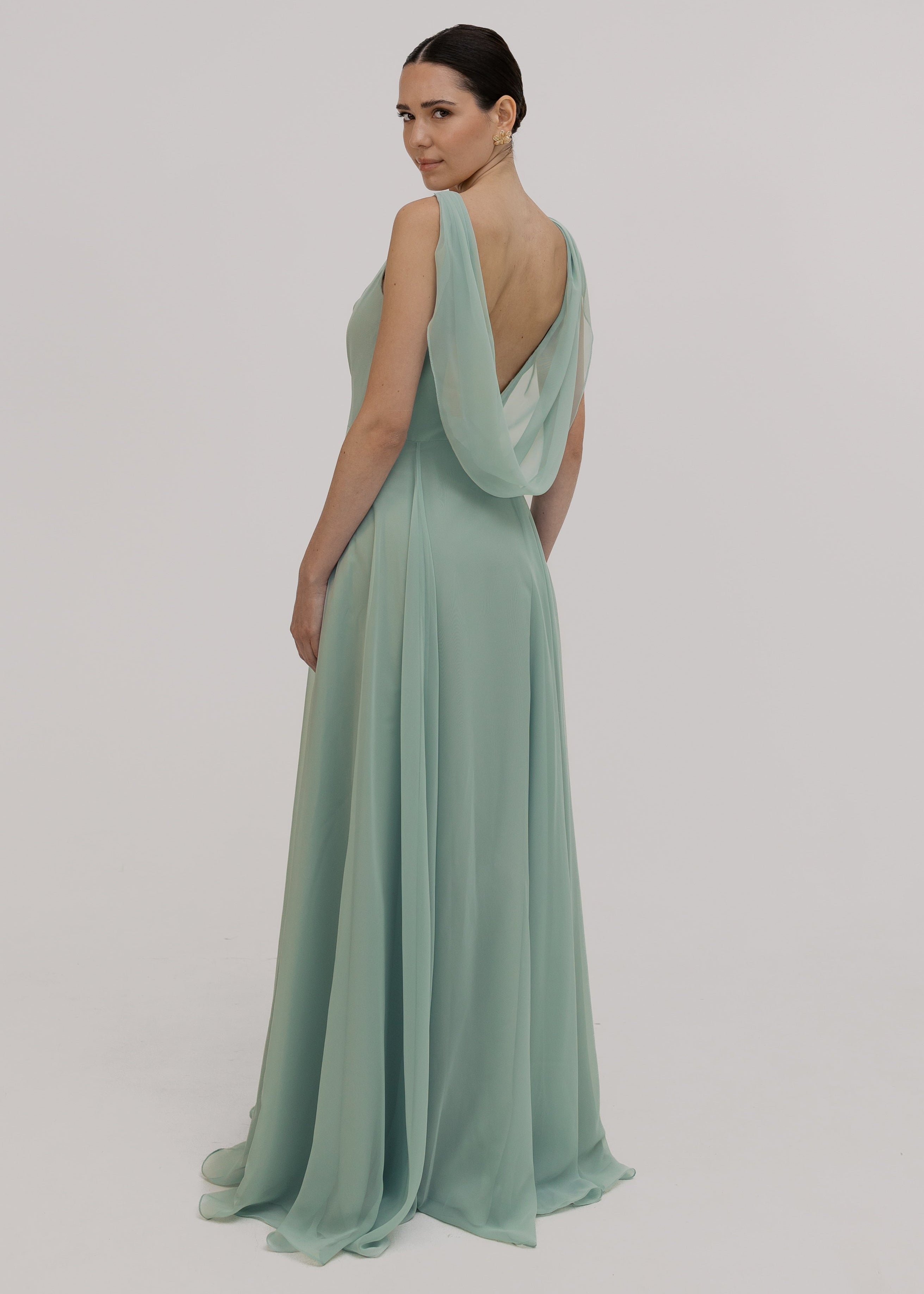 Model wearing a light green bridesmaid dress with a low cowl back on a plain background by TH&TH bridesmaids.