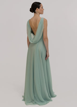 Woman wearing a light green gown with a flowing  cowl back design on a plain background by TH&TH bridesmaids.