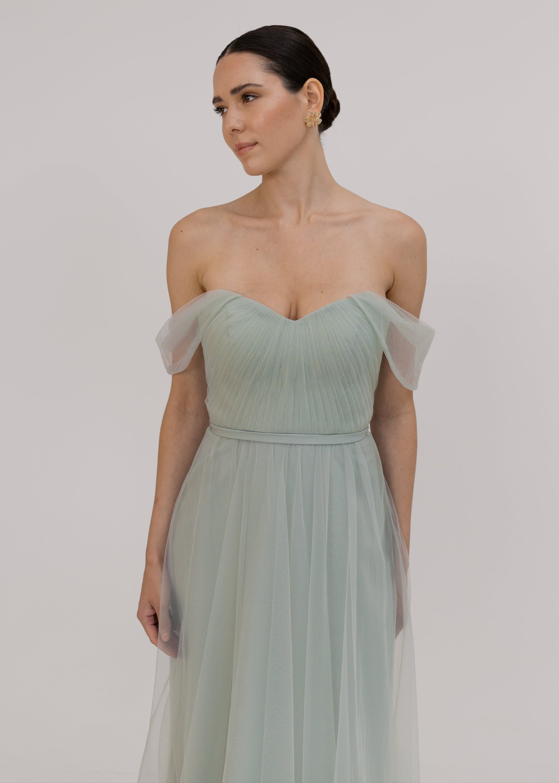 Woman wearing a light green strapless gown with sheer sleeves against a plain background by TH&TH Bridesmaids. 