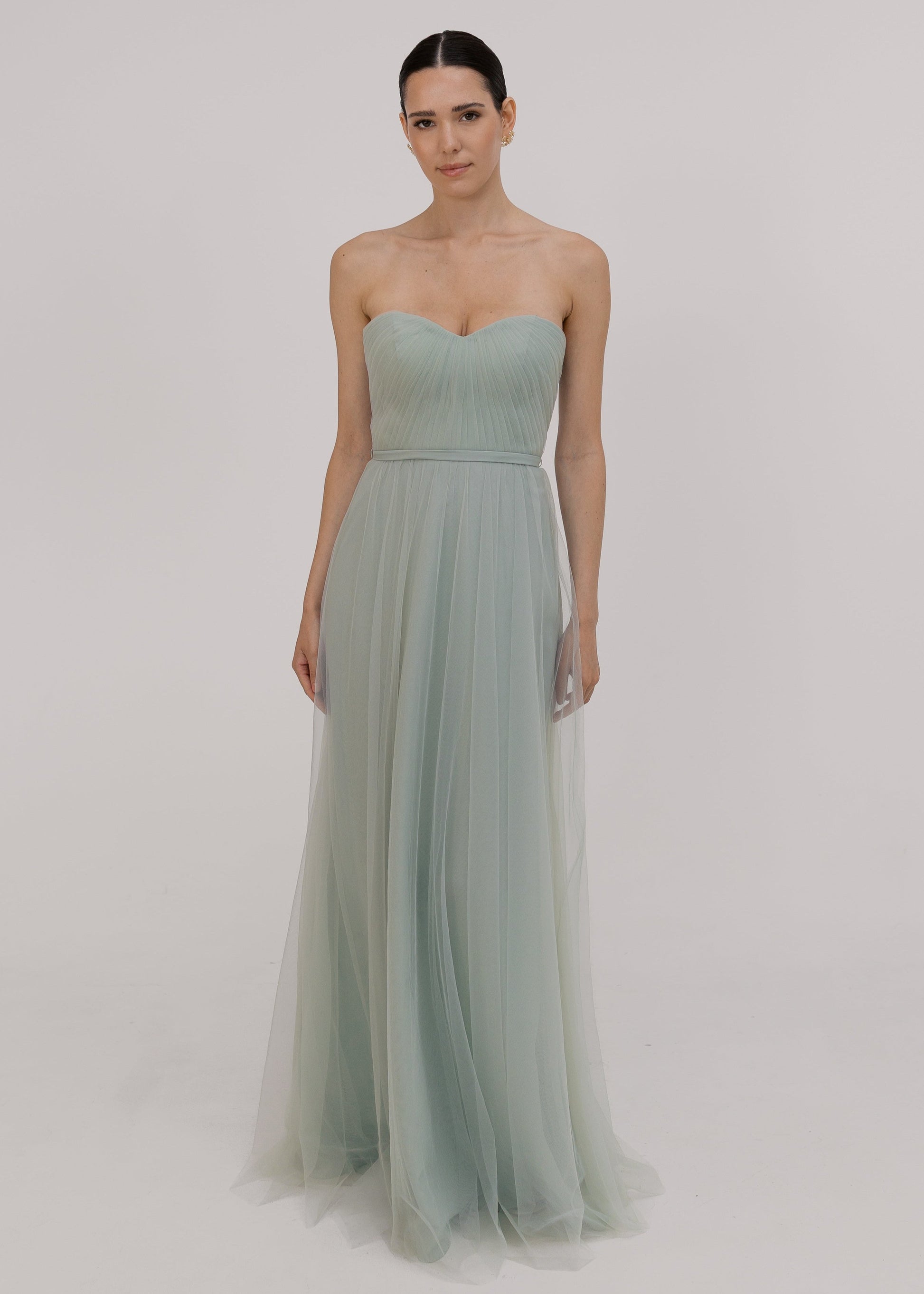 Model wears pleated strapless dress in light green against white ground by TH&TH bridesmaids.