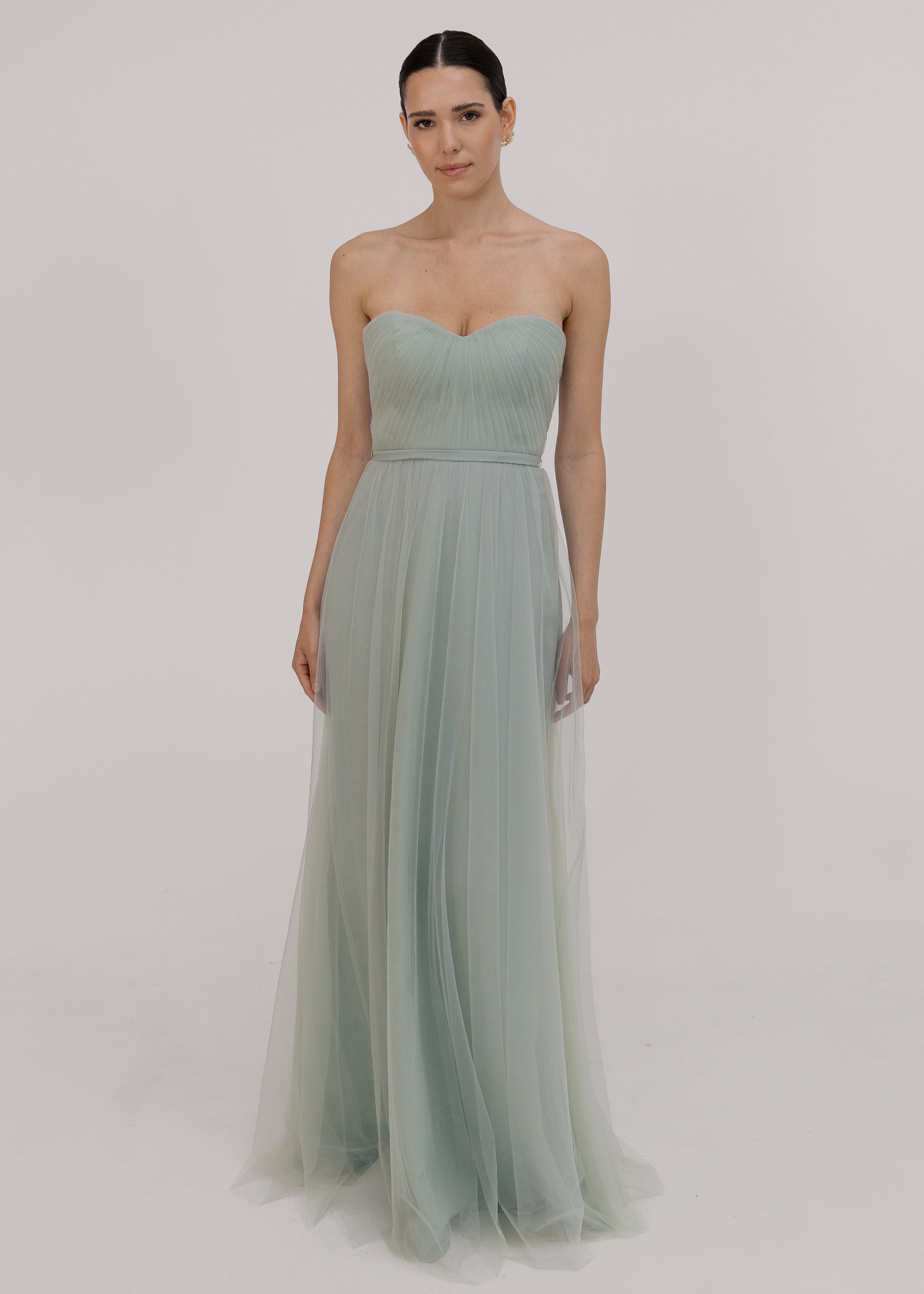 Model wears pleated strapless dress in light green against white ground by TH&TH bridesmaids.
