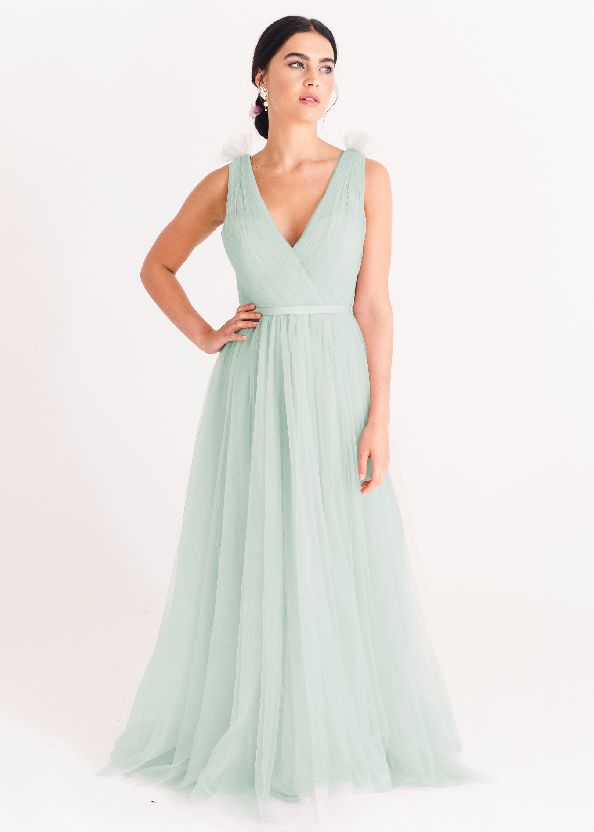 Model is wearing a green tulle bridesmaid dress by TH&TH Bridesmaids with her hand on hip and wearing earings. 