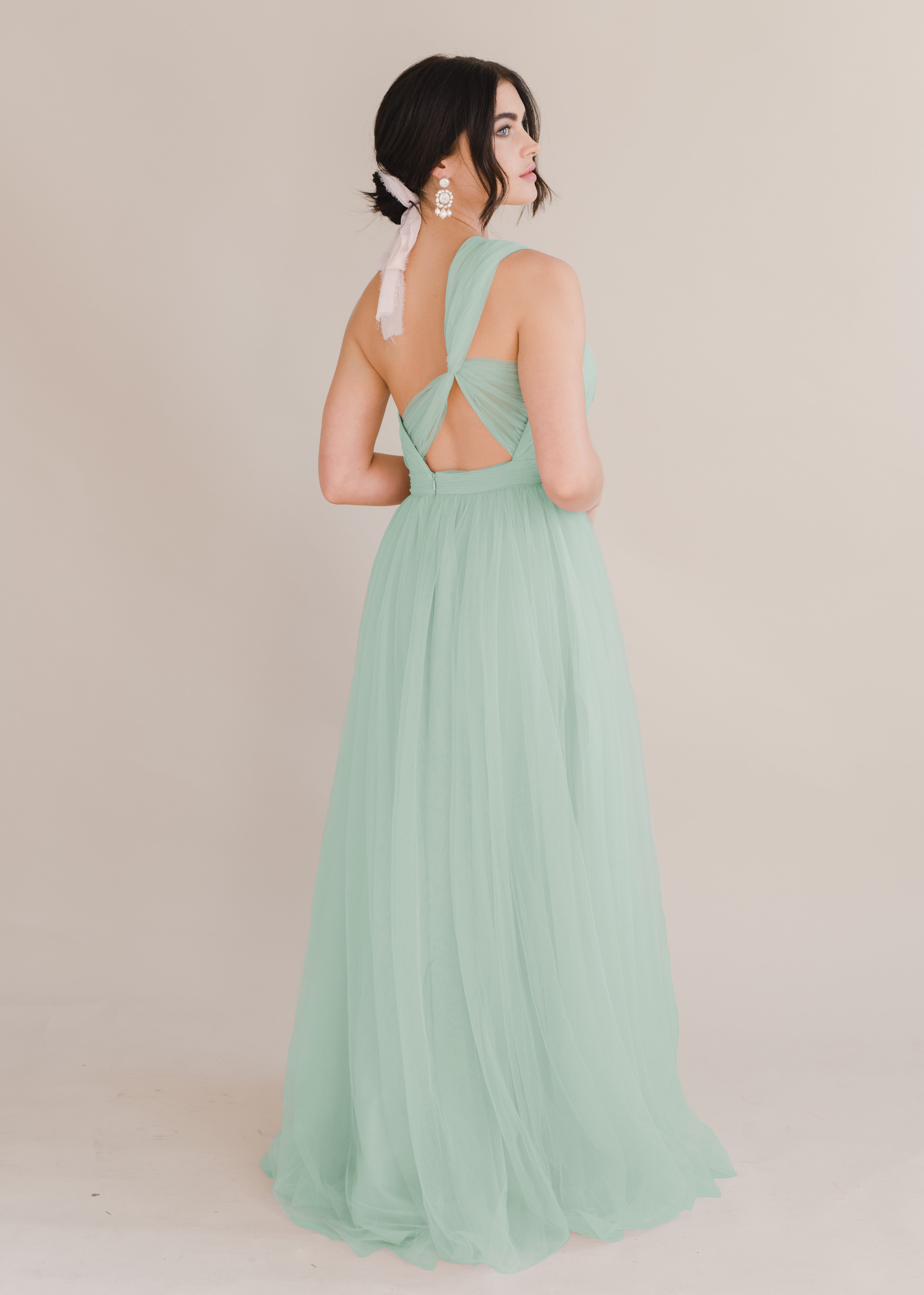 Woman wears TH&TH tulle dress in studio showing back detail with earings. 