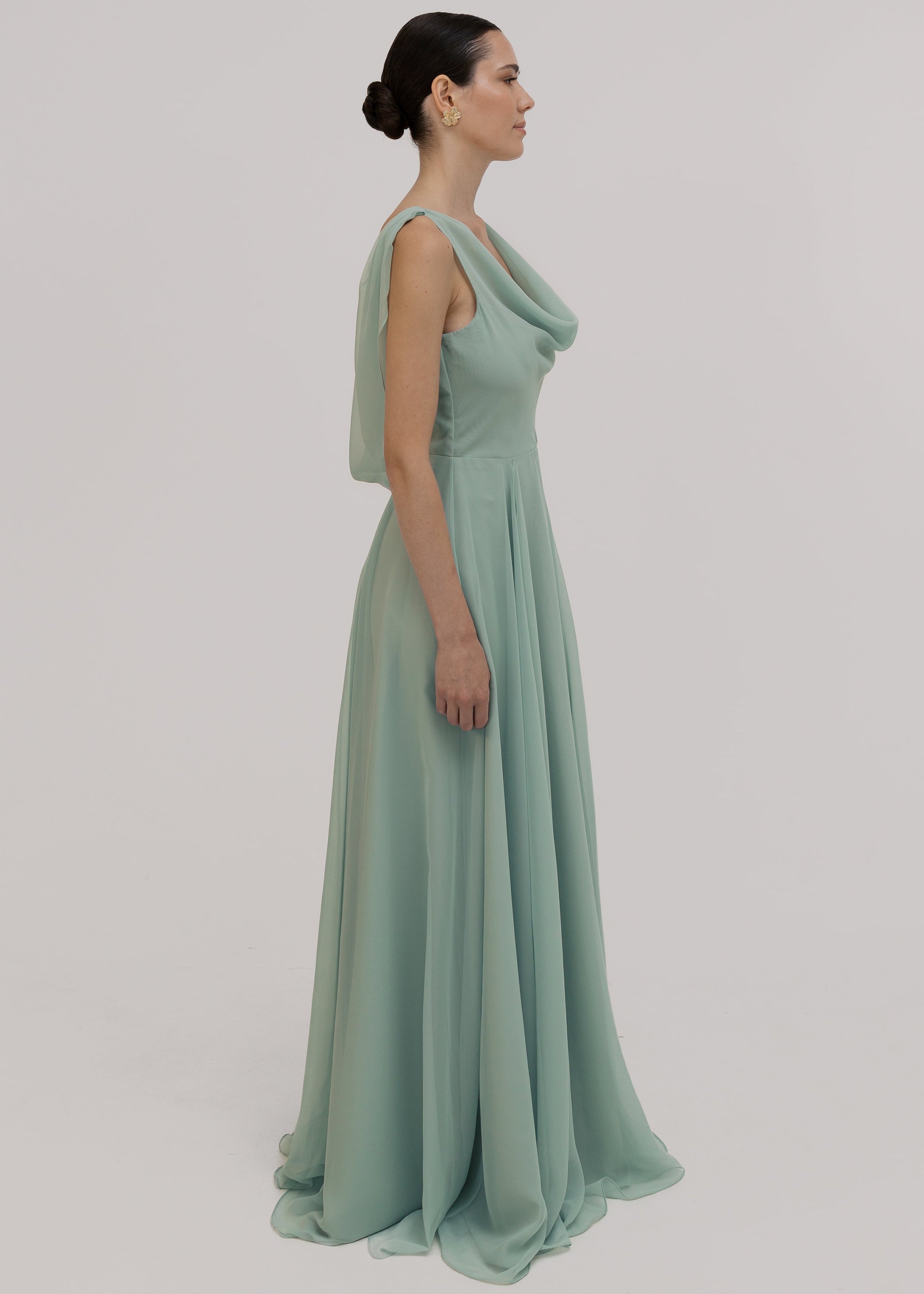 Woman wearing a light green bridesmaid dress with cowl neck and low back detail against a plain background by TH&TH Bridesmaids. 