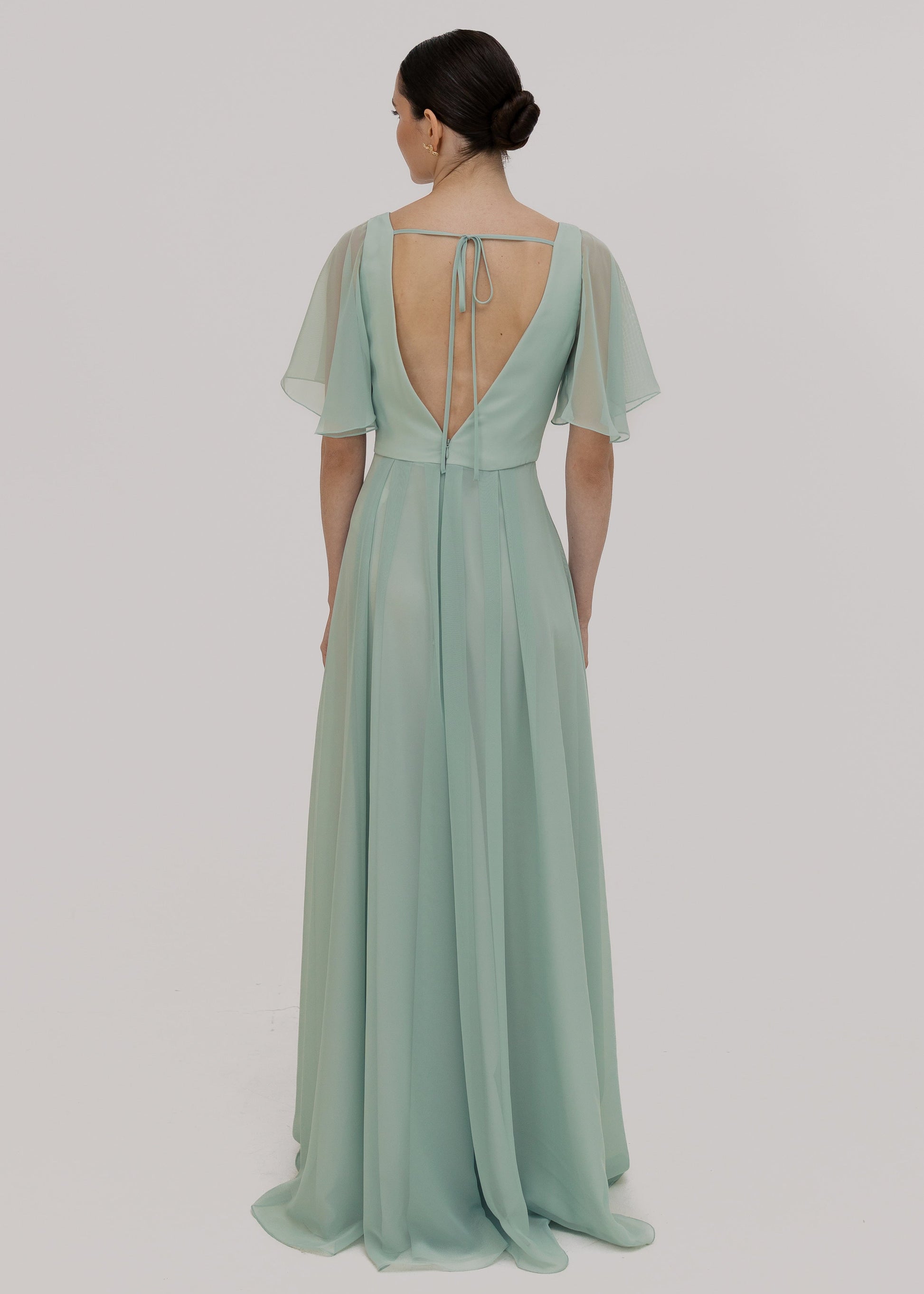 Woman wearing a light green dress with sheer flutter sleeves on a plain background by TH&TH Bridesmaids.