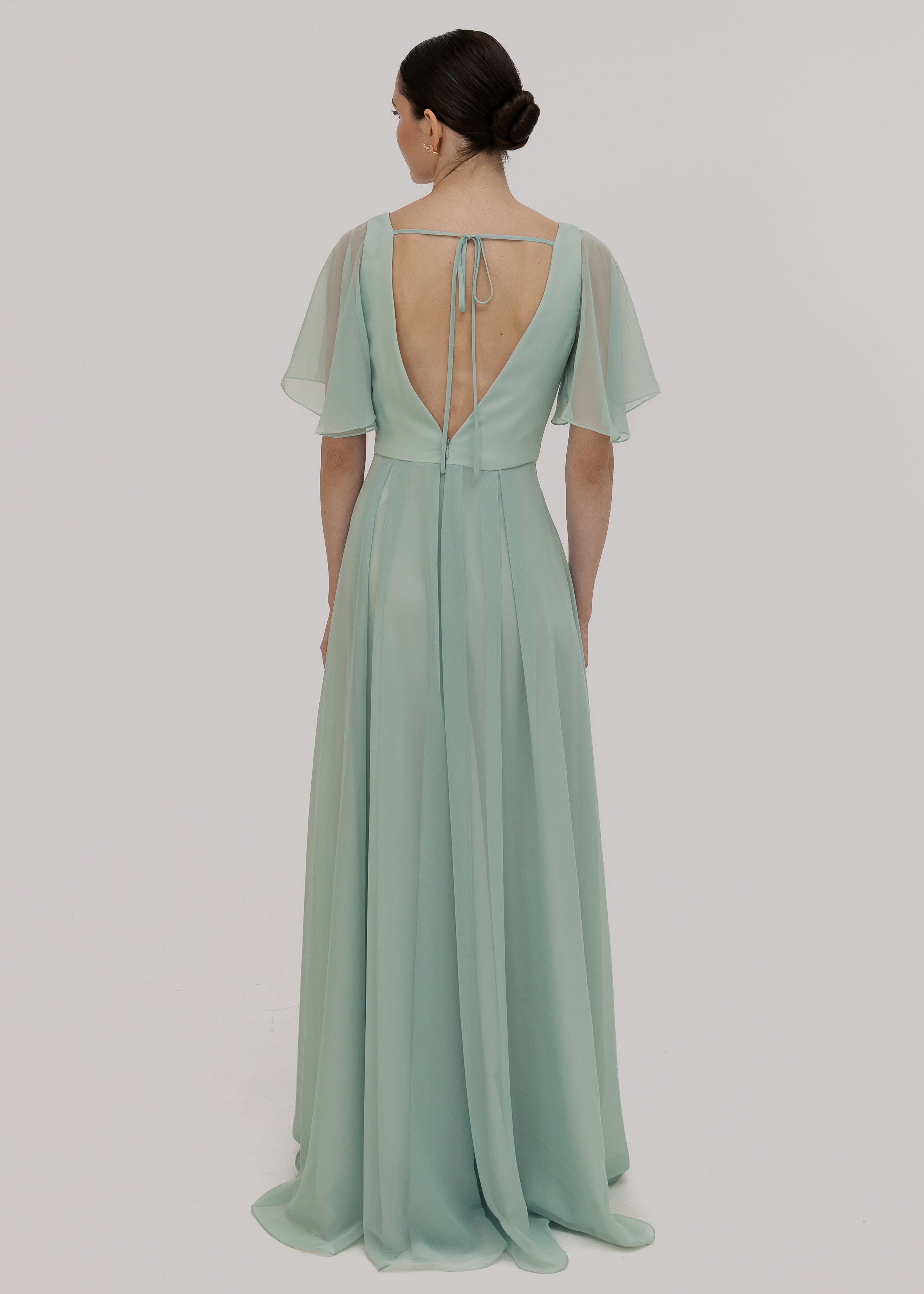Woman wearing a light green dress with sheer flutter sleeves on a plain background by TH&TH Bridesmaids.