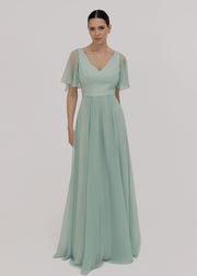 Woman wearing a light green dress with sheer flutter sleeves on a plain background by TH&TH Bridesmaids.