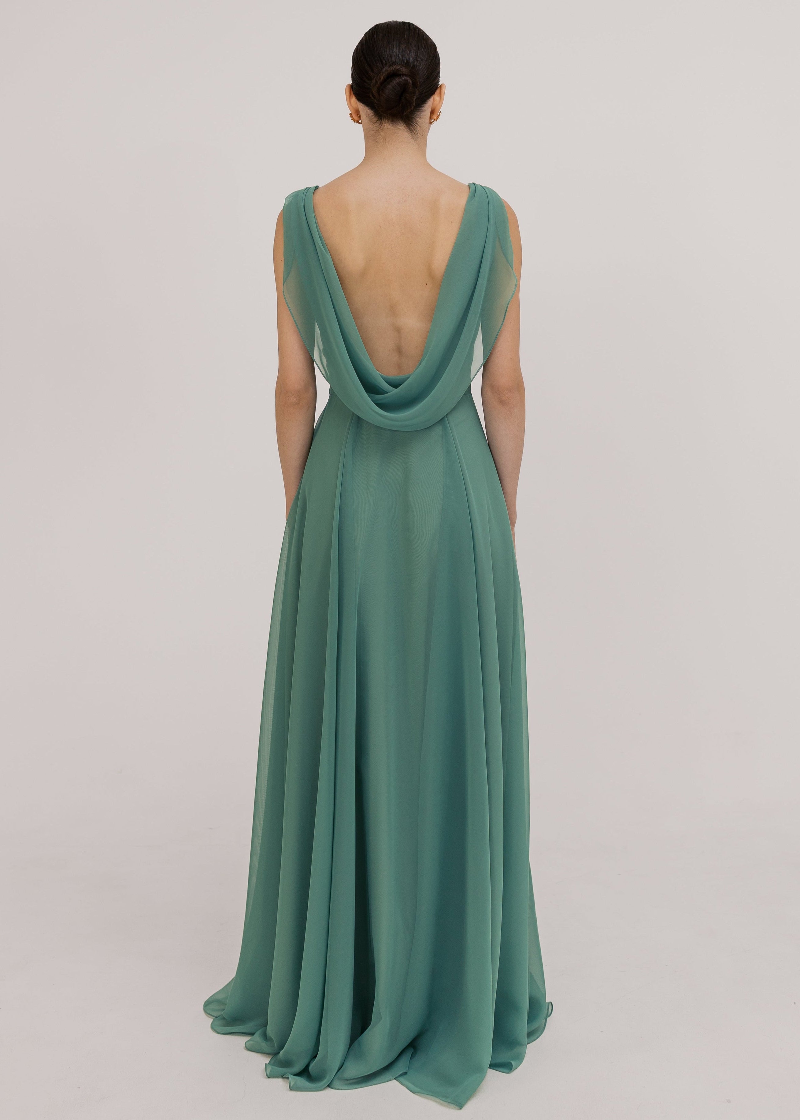 Model wearing a sage green bridesmaid dress with low cowl back detail and flowing chiffon skirt by TH&TH Bridesmaids.