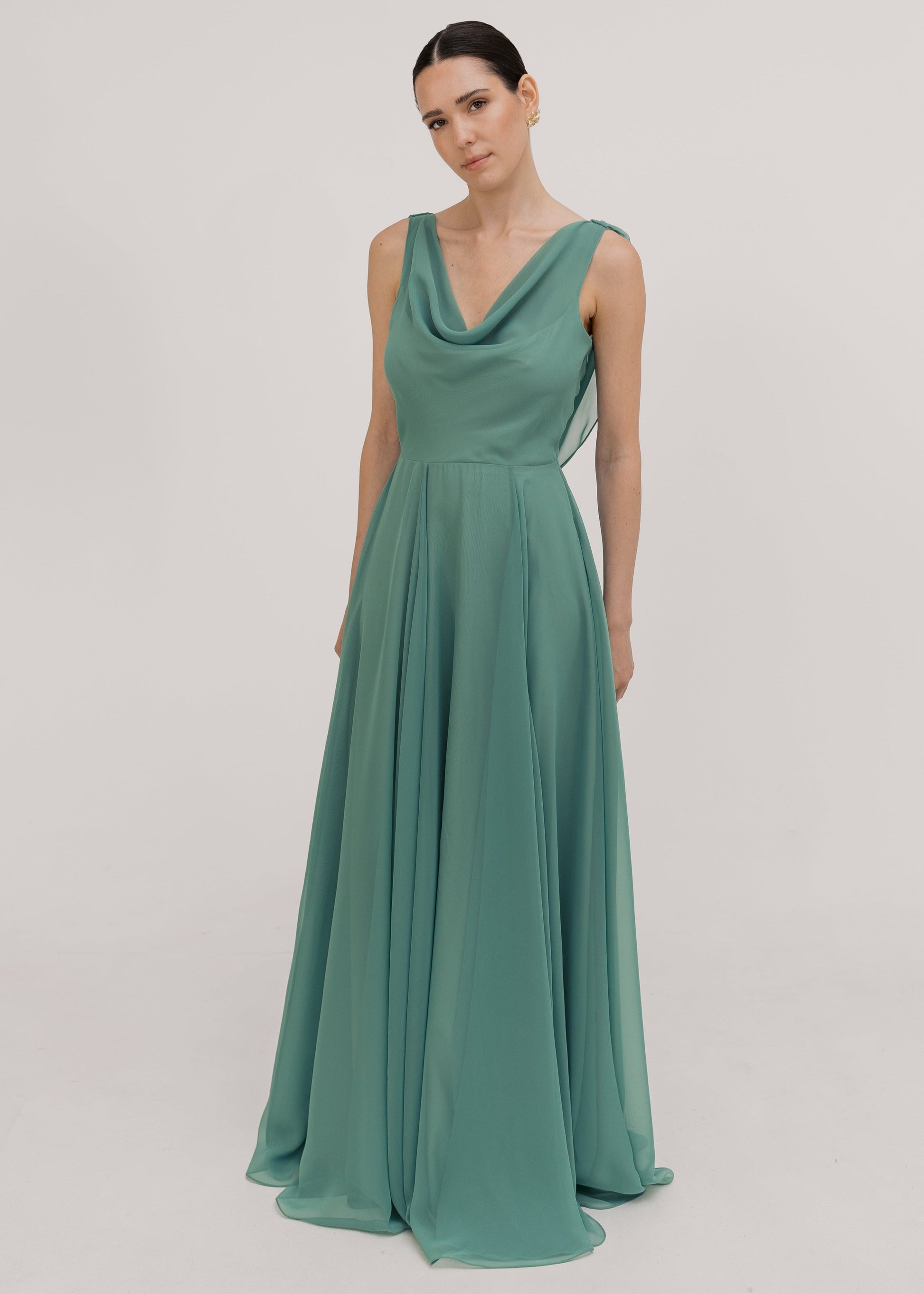 Model wearing a sage green bridesmaid dress in chiffon with cowl neckline and flowing chiffon skirt by TH&TH Bridesmaids. 