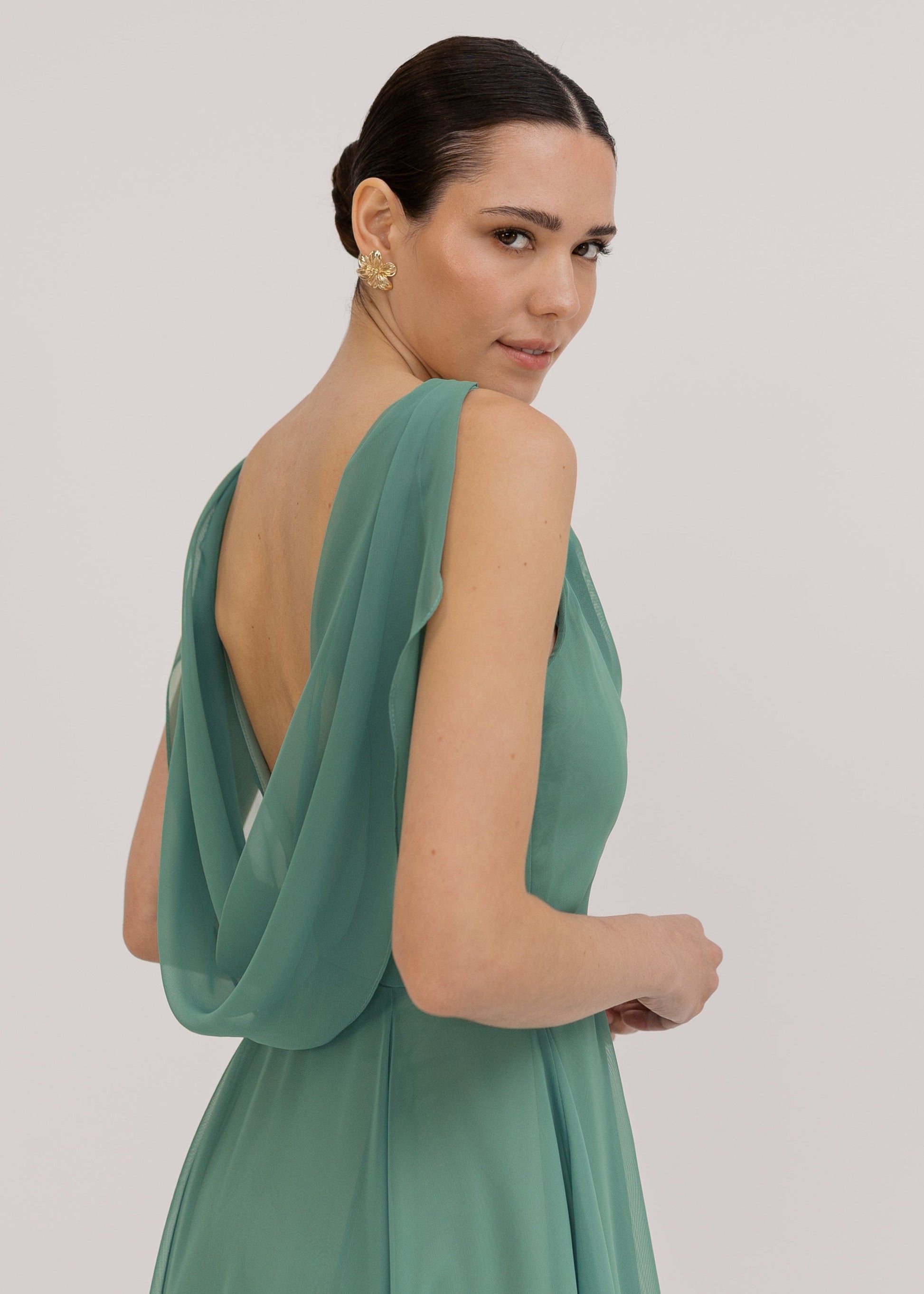 Model wearing a sage green bridesmaid dress in chiffon with low cowl back by TH&TH Bridesmaids. 