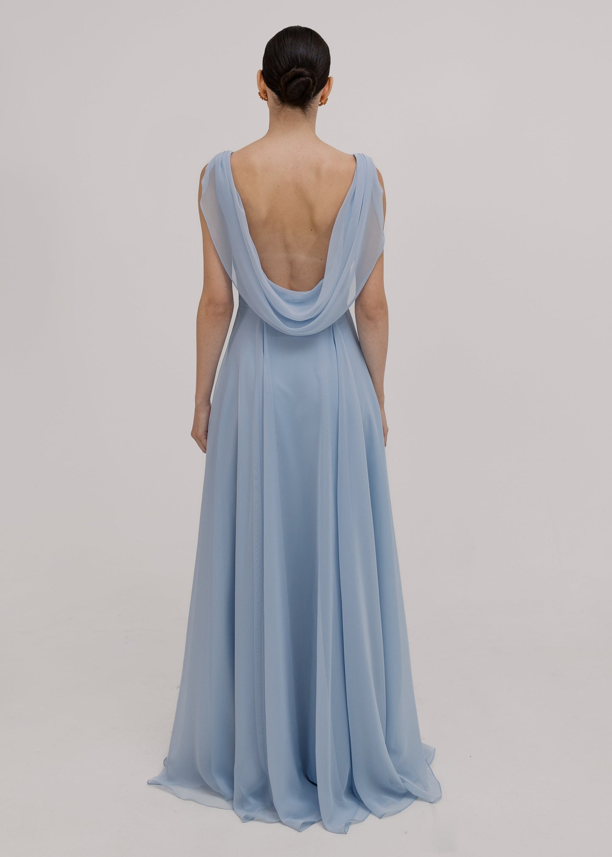 Model wearing a dusty blue bridesmaid dress in chiffon with low cowl back and flowing chiffon skirt by TH&TH Bridesmaids.

