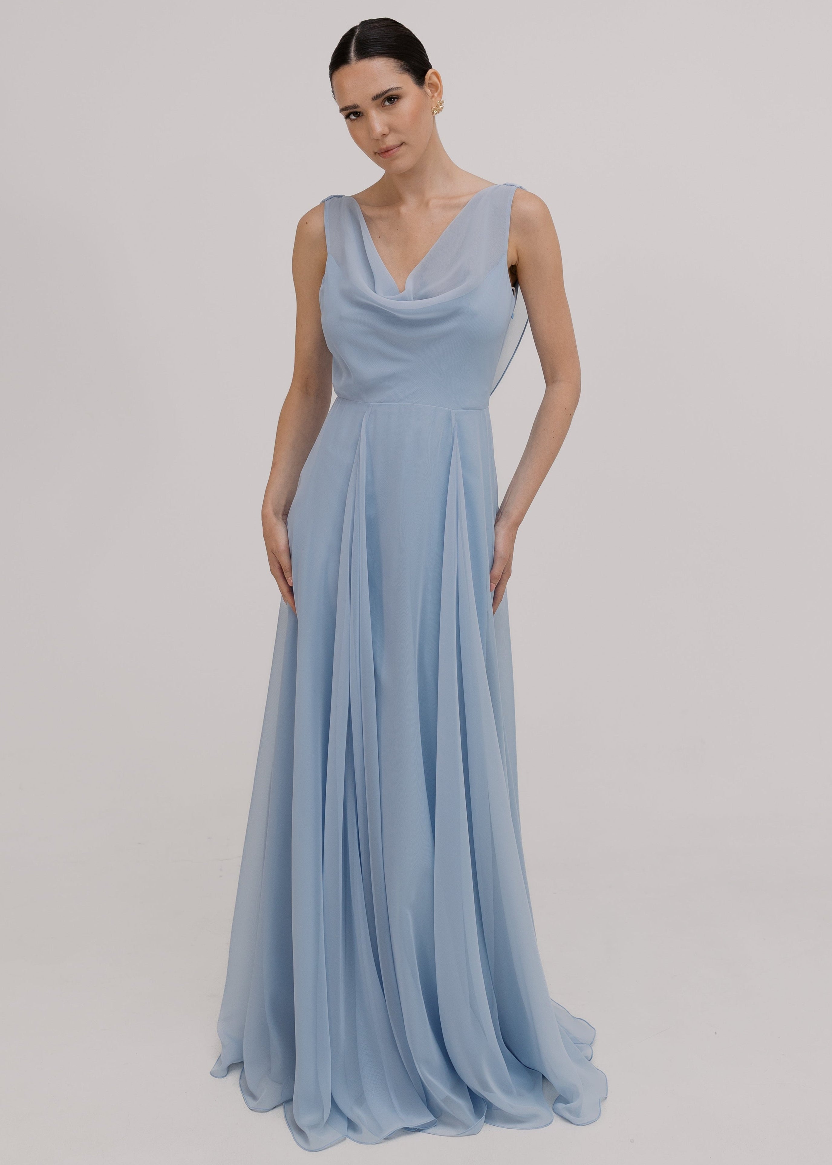 Model wearing a dusty blue bridesmaid dress in chiffon with cowl neckline and flowing chiffon skirt by TH&TH Bridesmaids.
